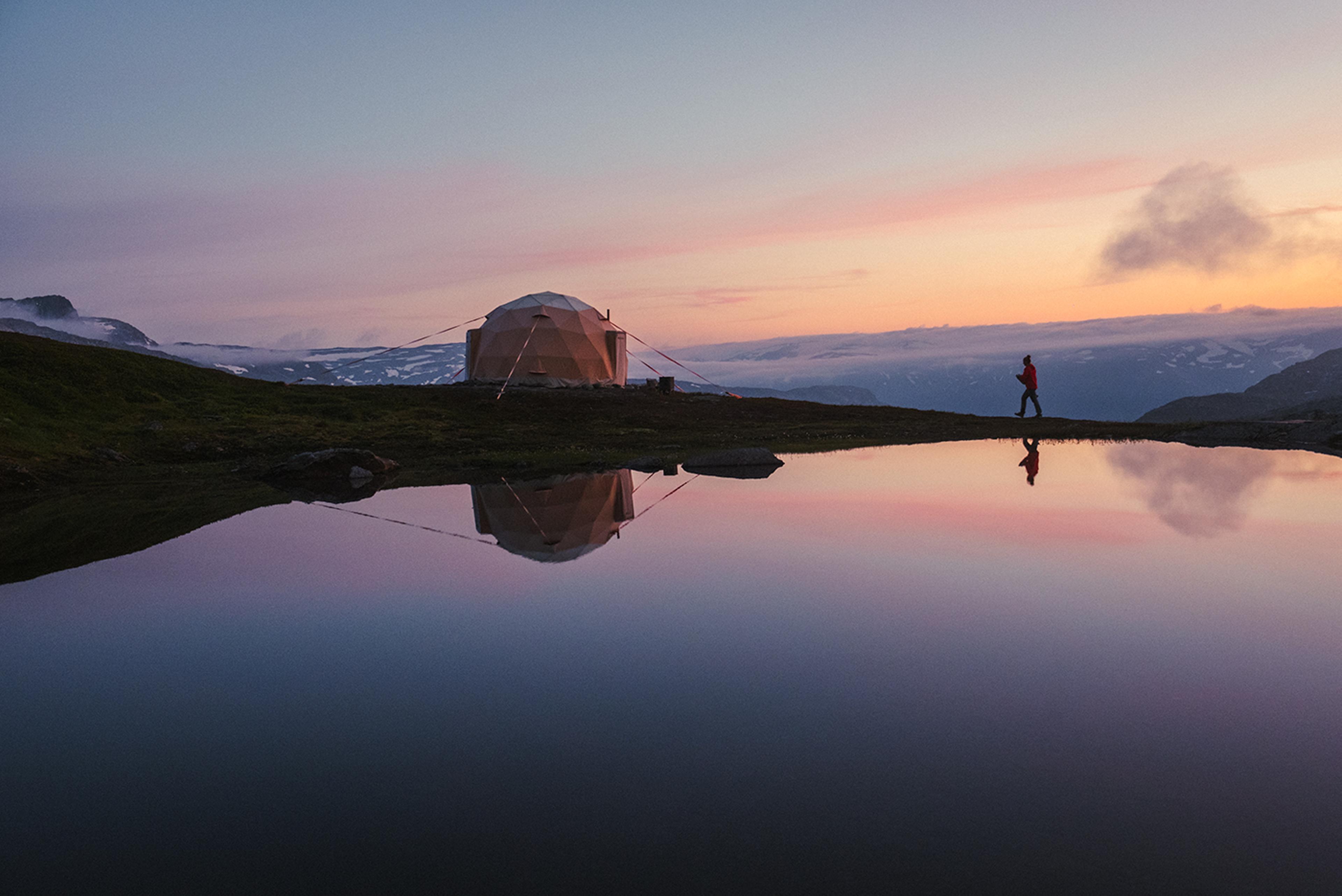 Geodesic glamping dome by a calm mountain lake at sunset near Trolltunga, Hardanger.
