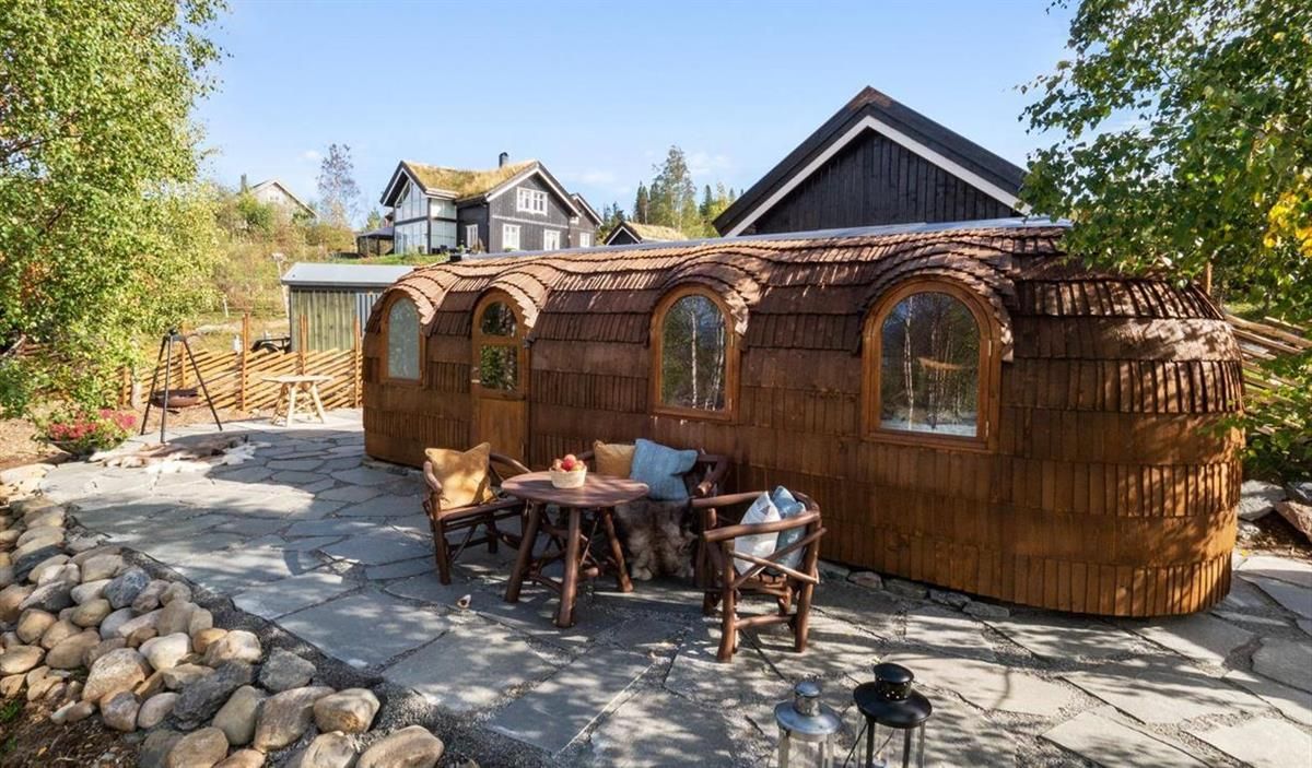 En uteplass med trebygninger og sittegruppe omgitt av stein og trær.