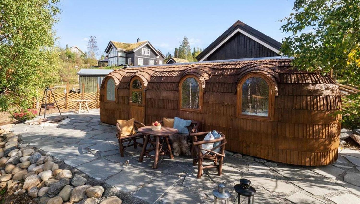 En uteplass med trebygninger og sittegruppe omgitt av stein og trær.