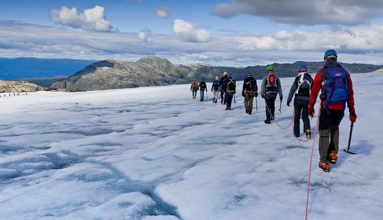 A group of hikers walking across the Folgefonna Glacier in Hardanger, led by a glacier guide with an ice axe and crampons.