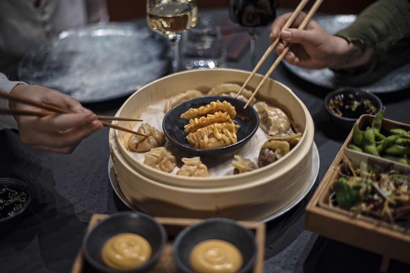 Two persons holding chopsticks picking up food from a table decked with various dishes