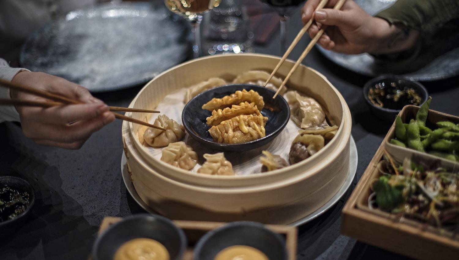 Two persons holding chopsticks picking up food from a table decked with various dishes