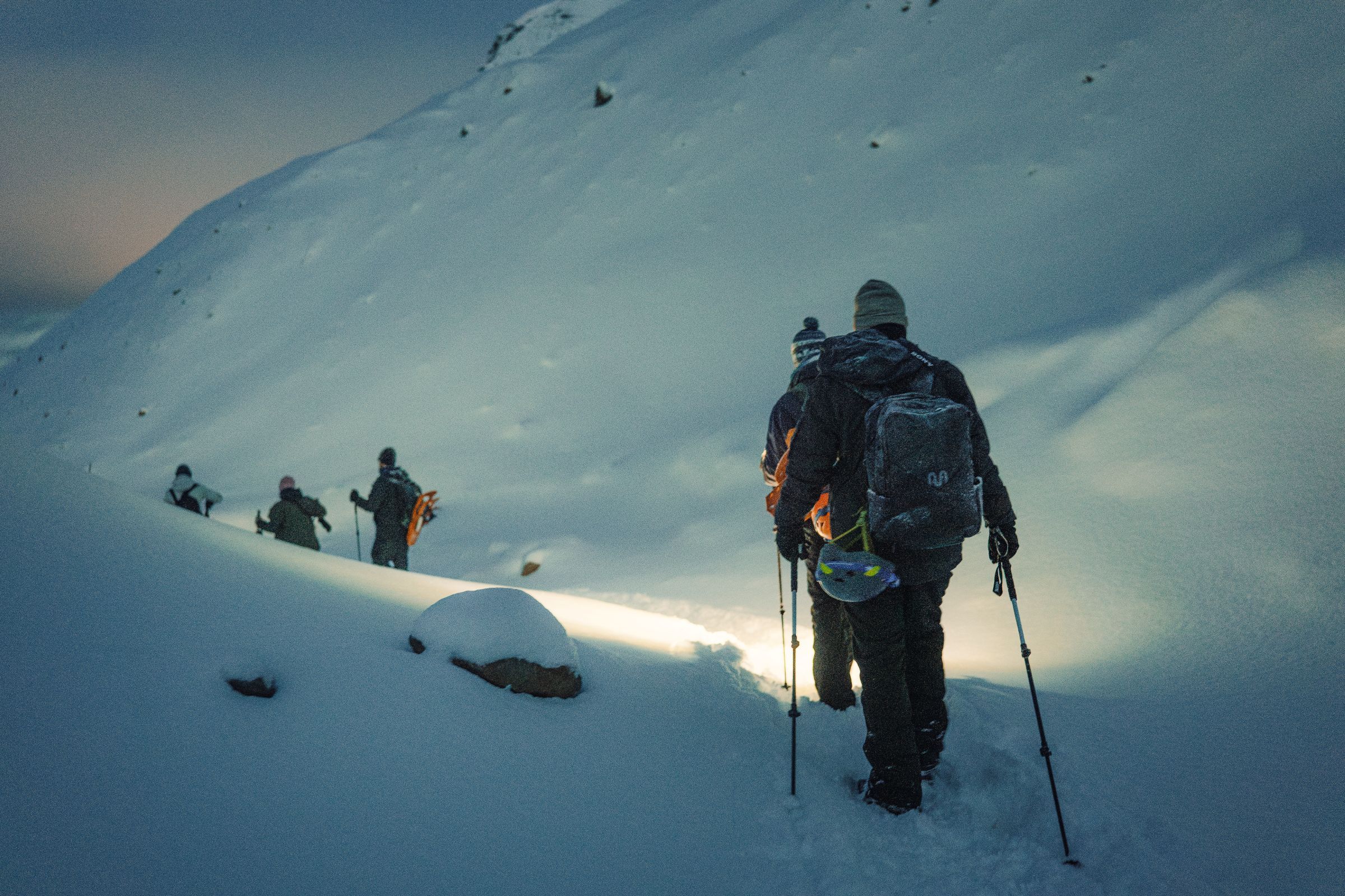 A group of people walking down a snow covered mountain