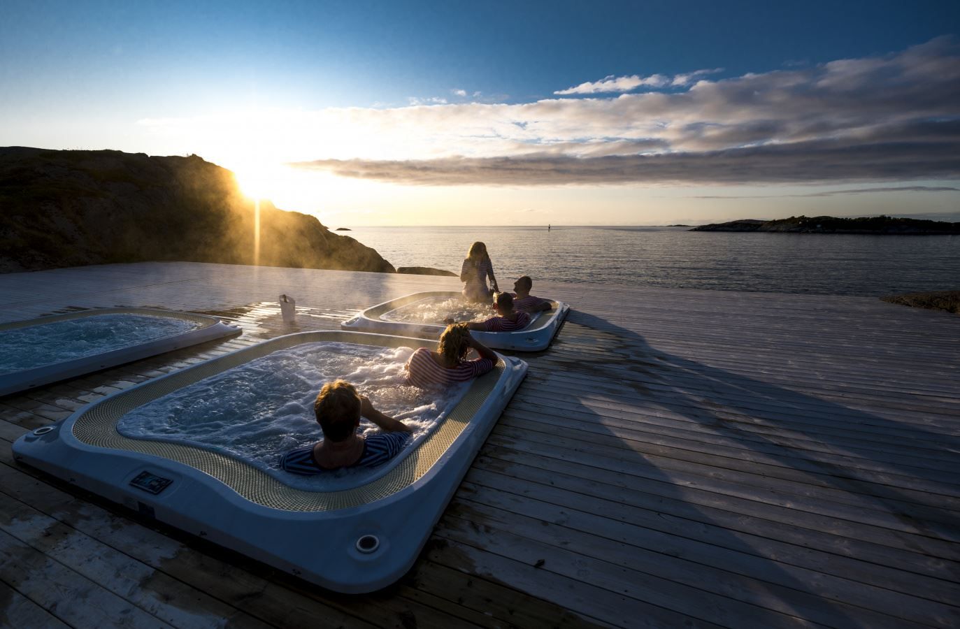 utendørs boblebad med utsikt over fjorden, med midnattssolen som går ned i horisonten