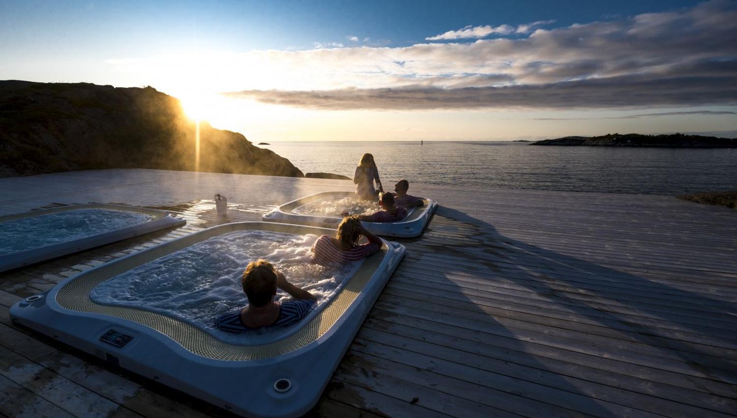 utendørs boblebad med utsikt over fjorden, med midnattssolen som går ned i horisonten