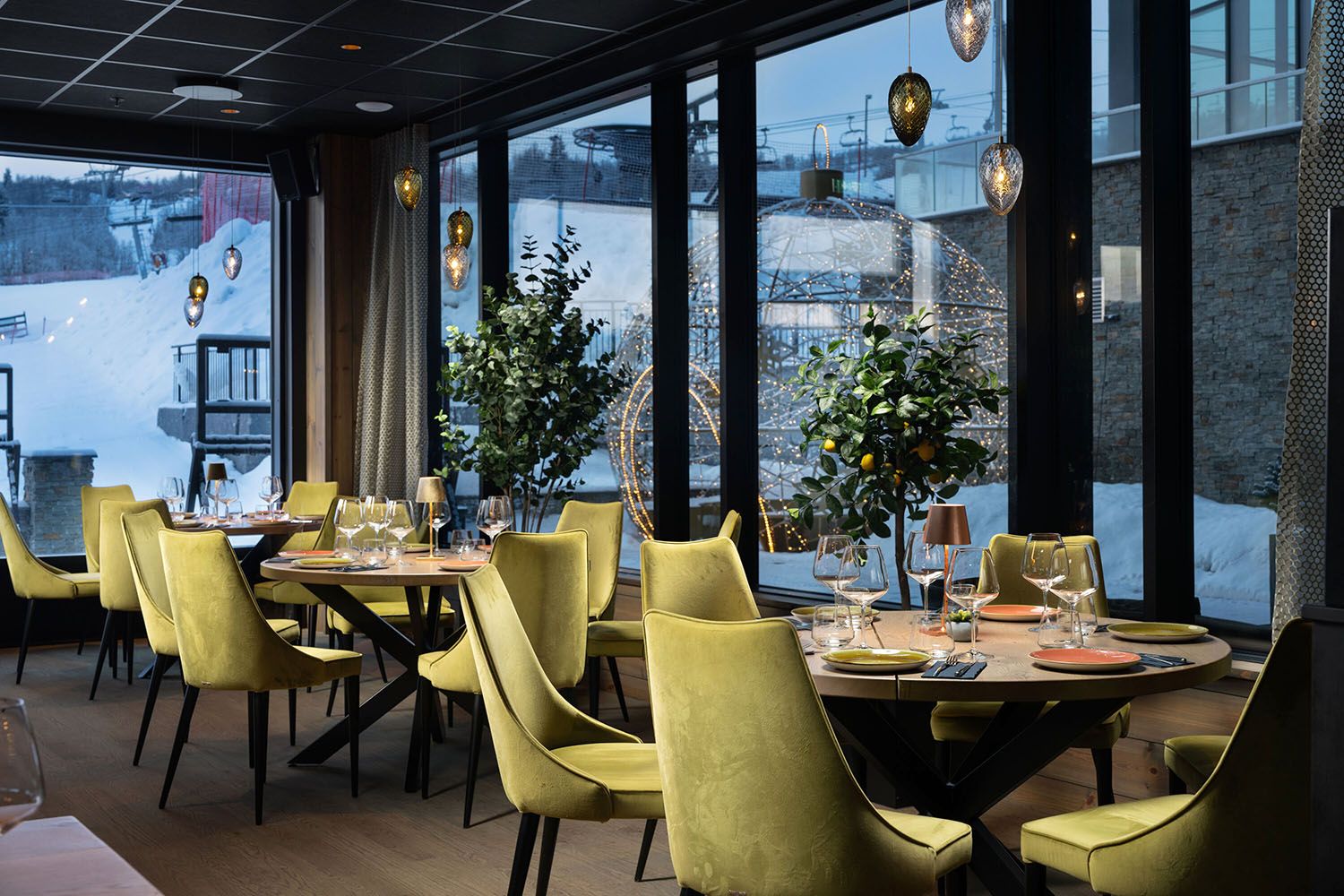 Restaurantinnredning med lysegrønne polsterstoler og varm belysning. Ute er det snø.