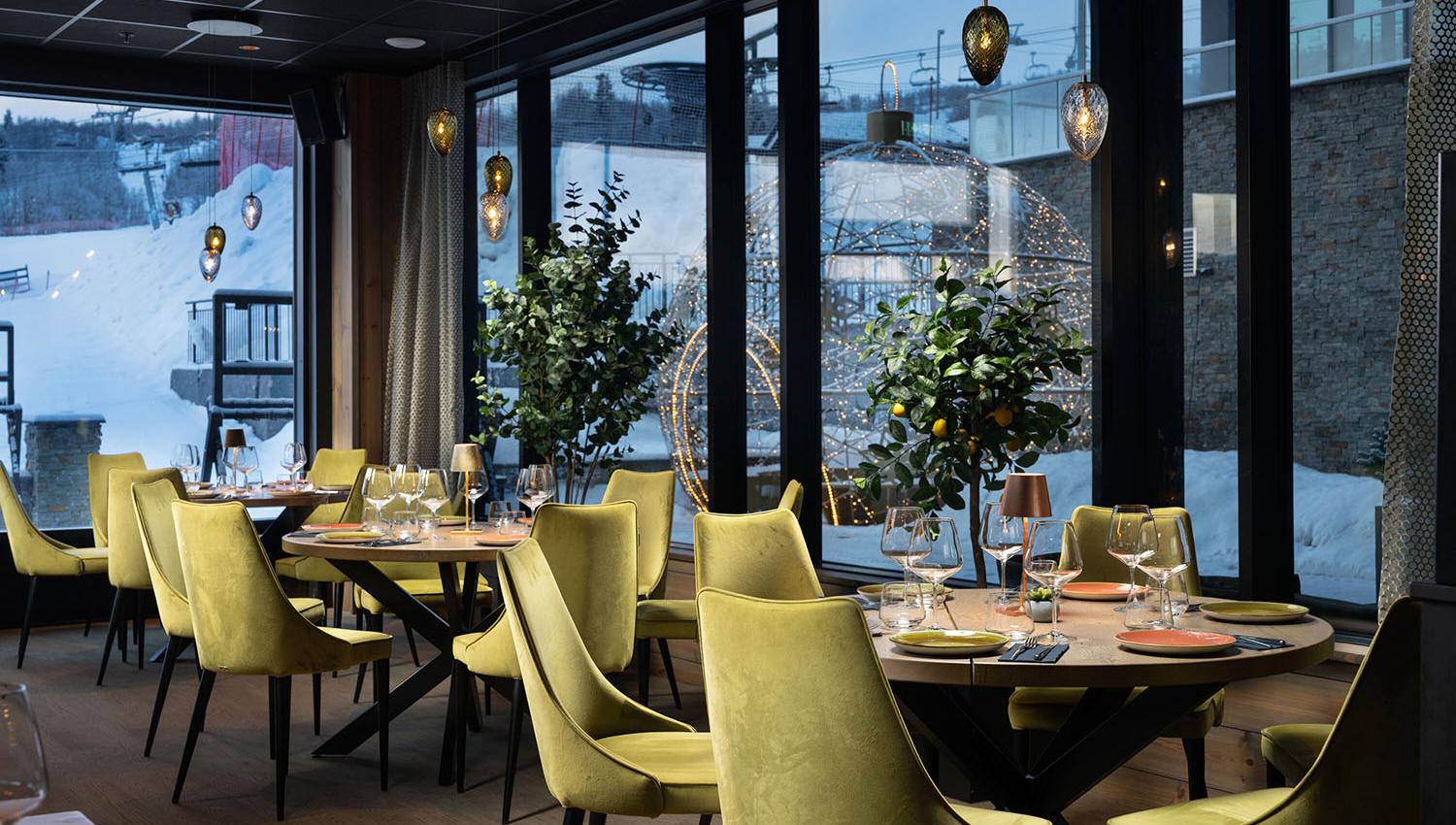 Restaurantinnredning med lysegrønne polsterstoler og varm belysning. Ute er det snø.