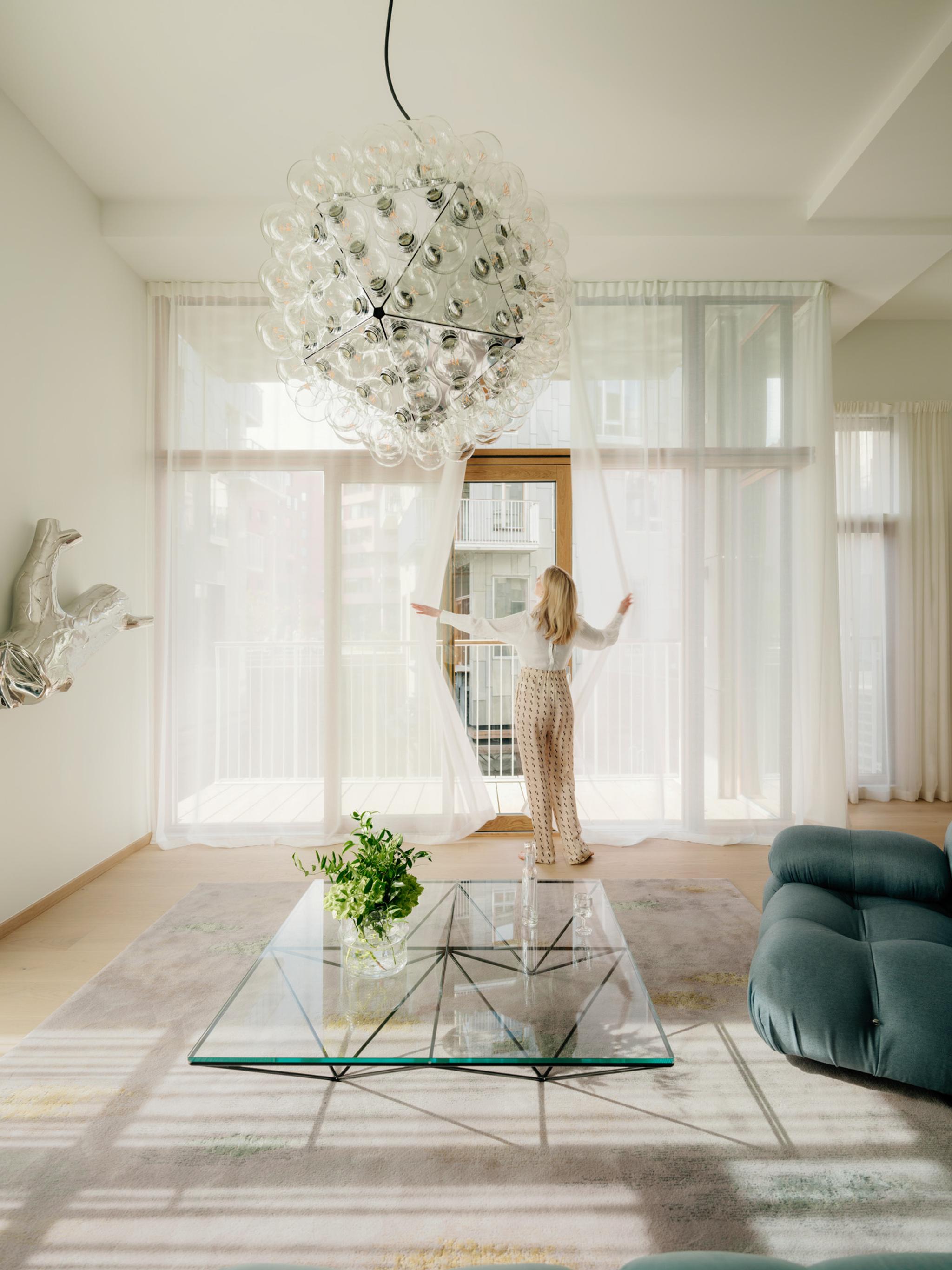 Lady in white living room with large panoramic windows pulling the curtains aside