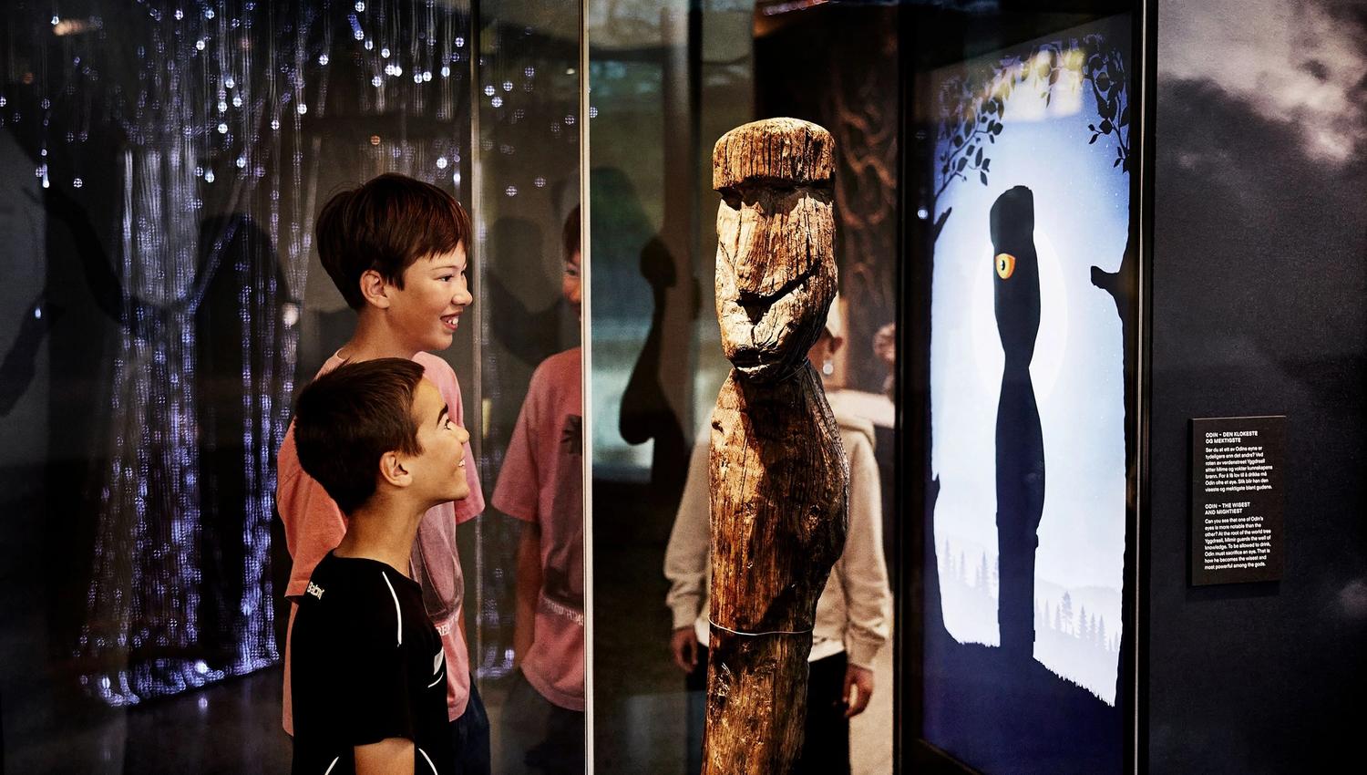 Two children looking at a wooden figure of Odin on display