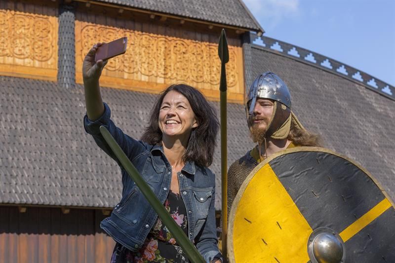 A lady and a man dressed as a Viking stand in front of the Gildehallen and take a selfie.