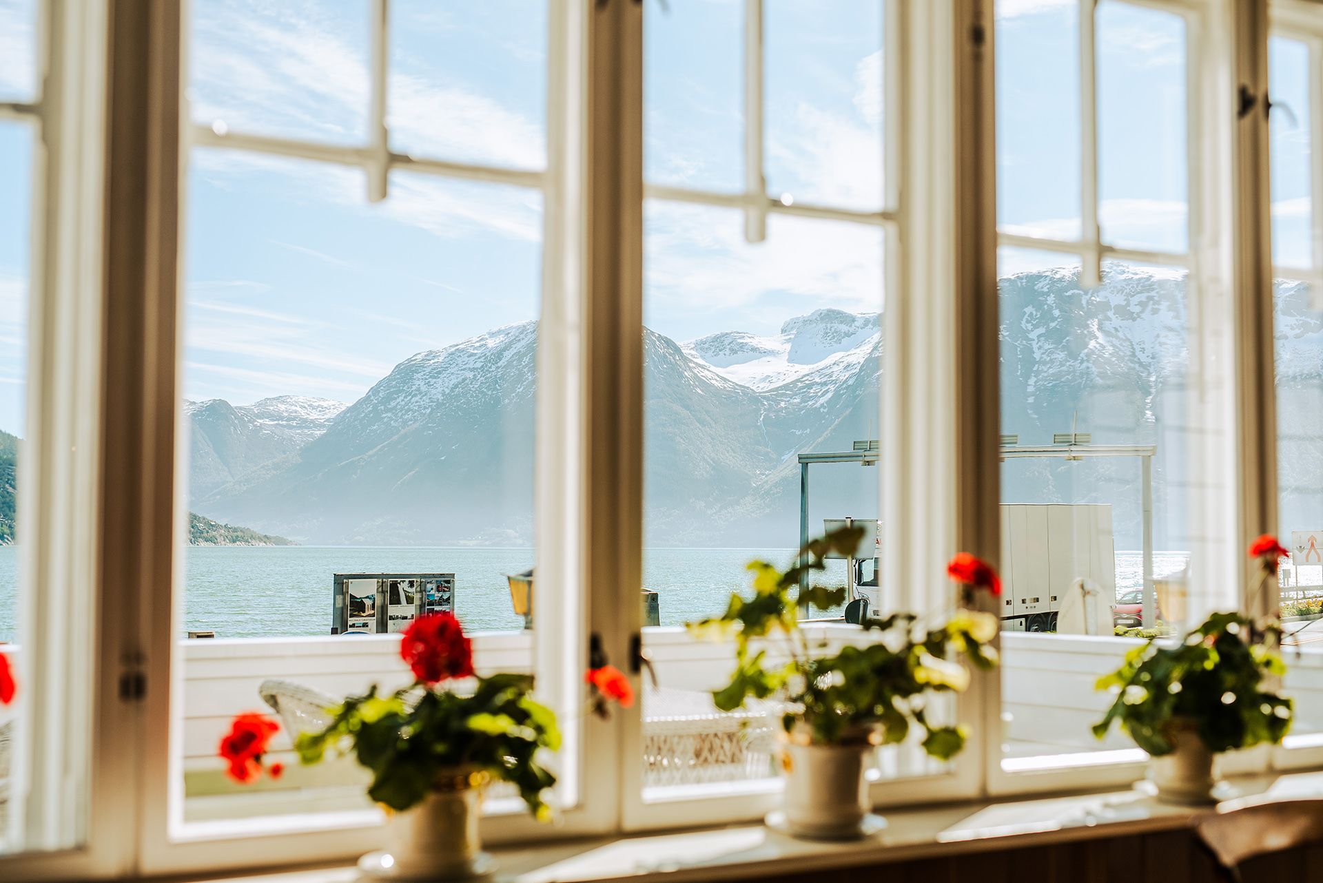 Panoramic view of the Hardangerfjord from a window at Utne Hotel, framed by red geraniums.