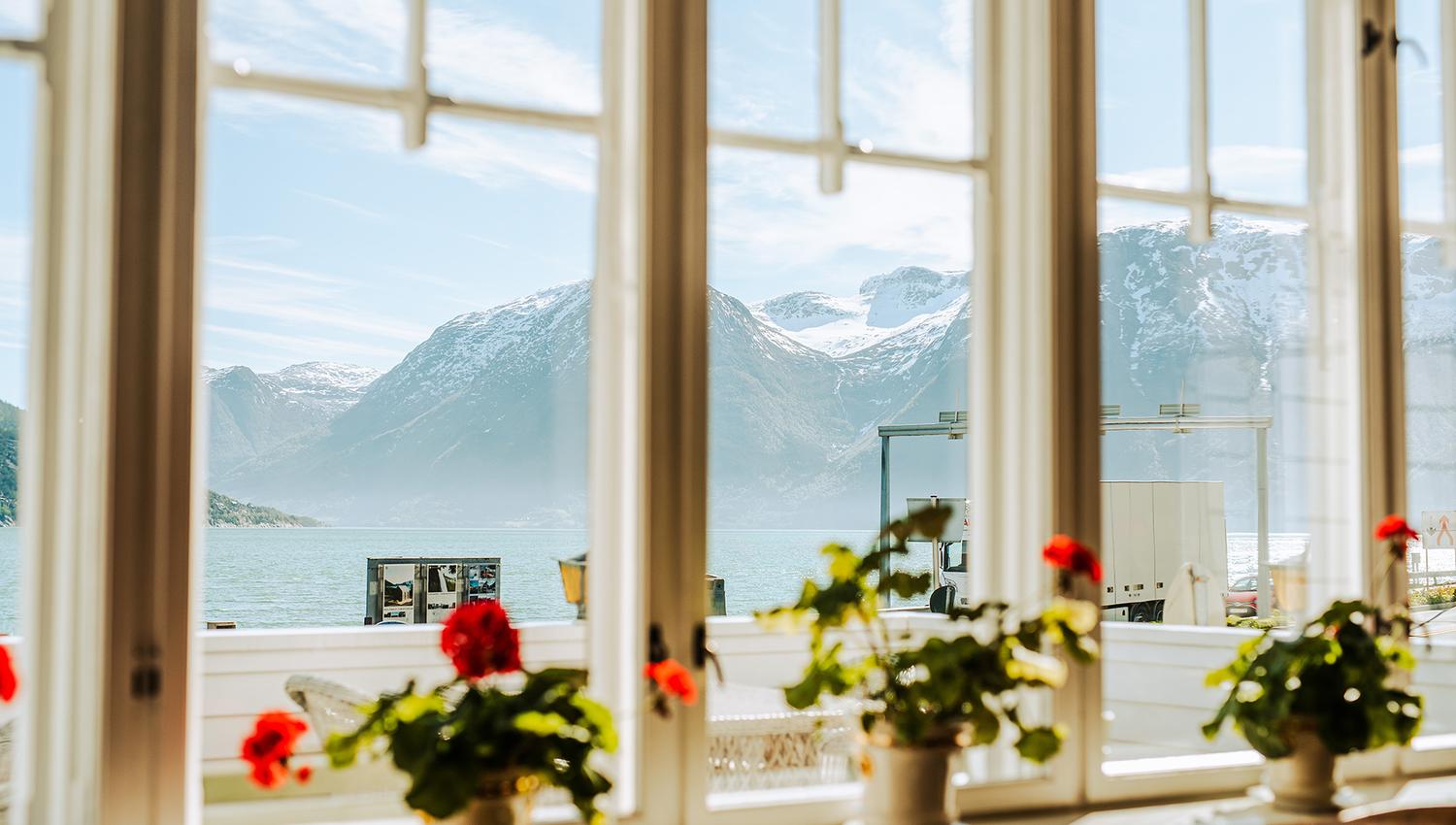 Panoramic view of the Hardangerfjord from a window at Utne Hotel, framed by red geraniums.