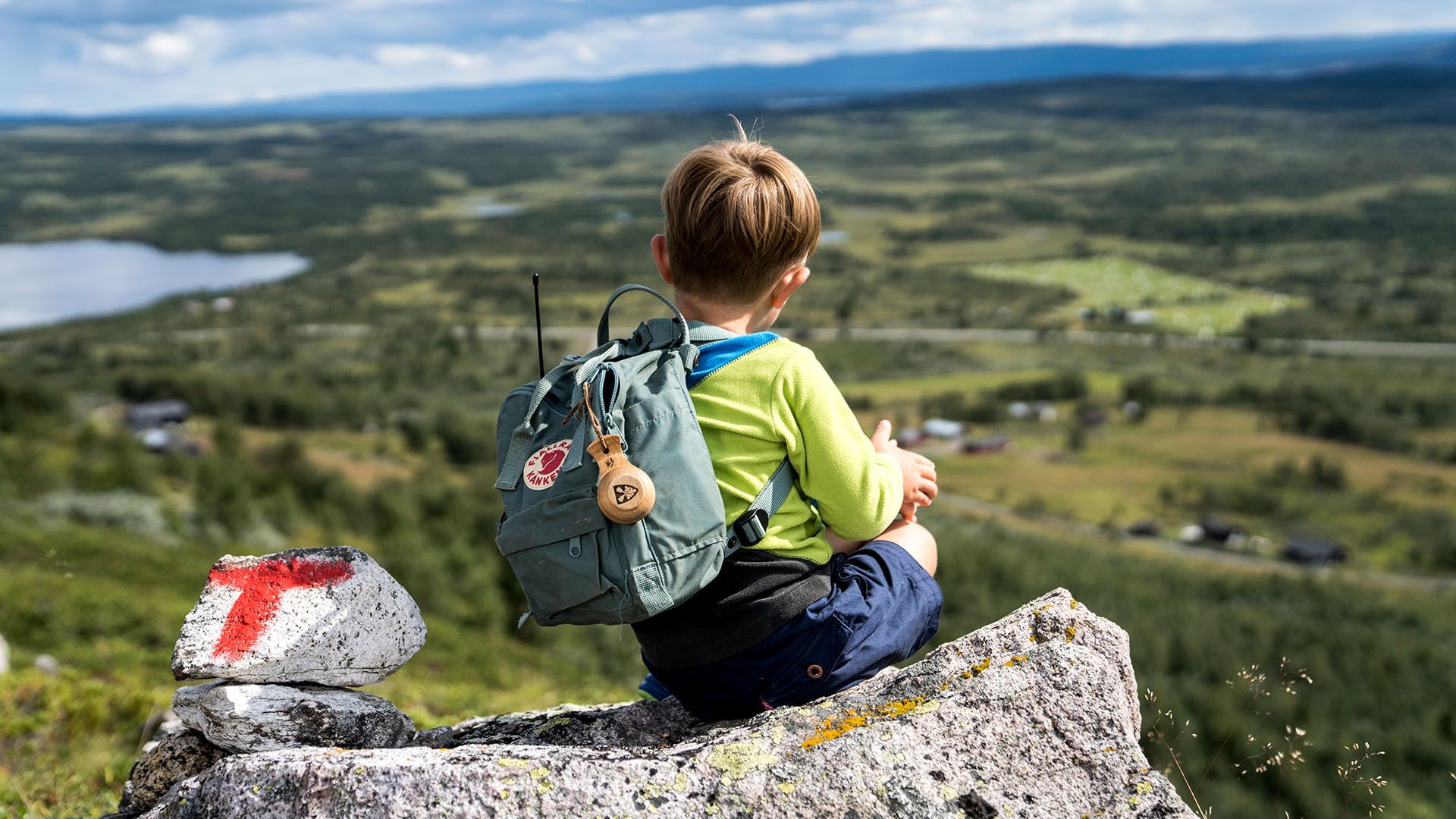 Liten gutt tar en pause på en stein ved siden av en rødmalt T - som viser at dette er en DNT-sti. Storslått utsikt.