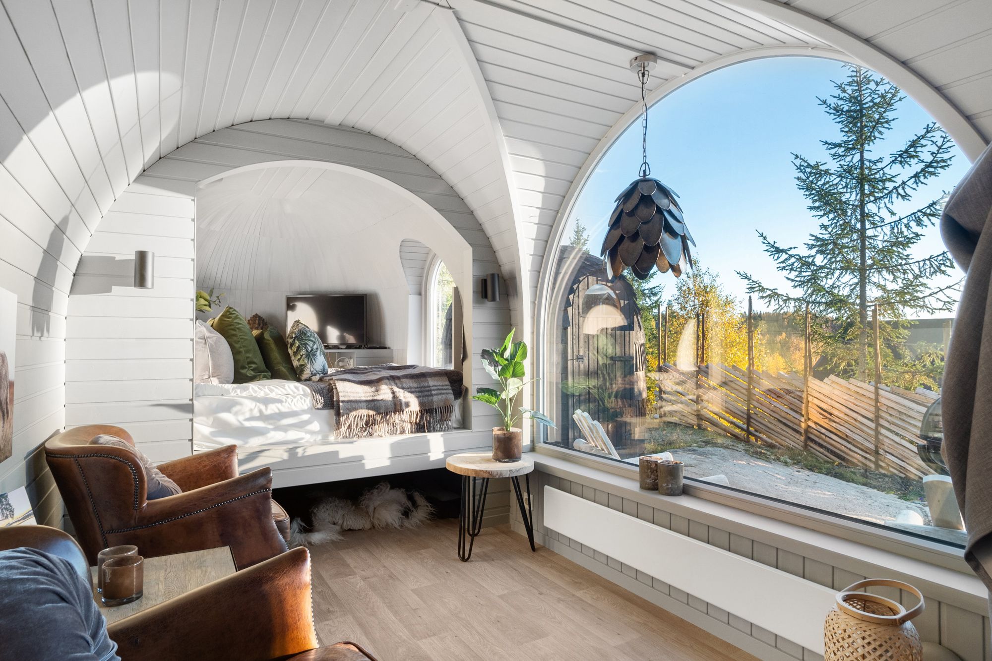 Innteriør bilde fra en hytte med stort vindu, stoler og seng og utsikt