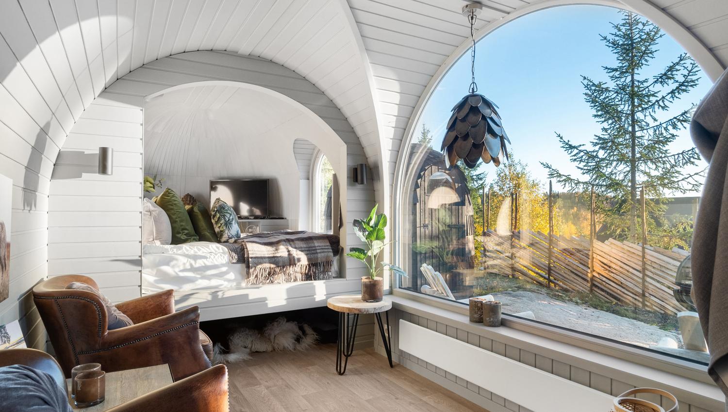 Innteriør bilde fra en hytte med stort vindu, stoler og seng og utsikt