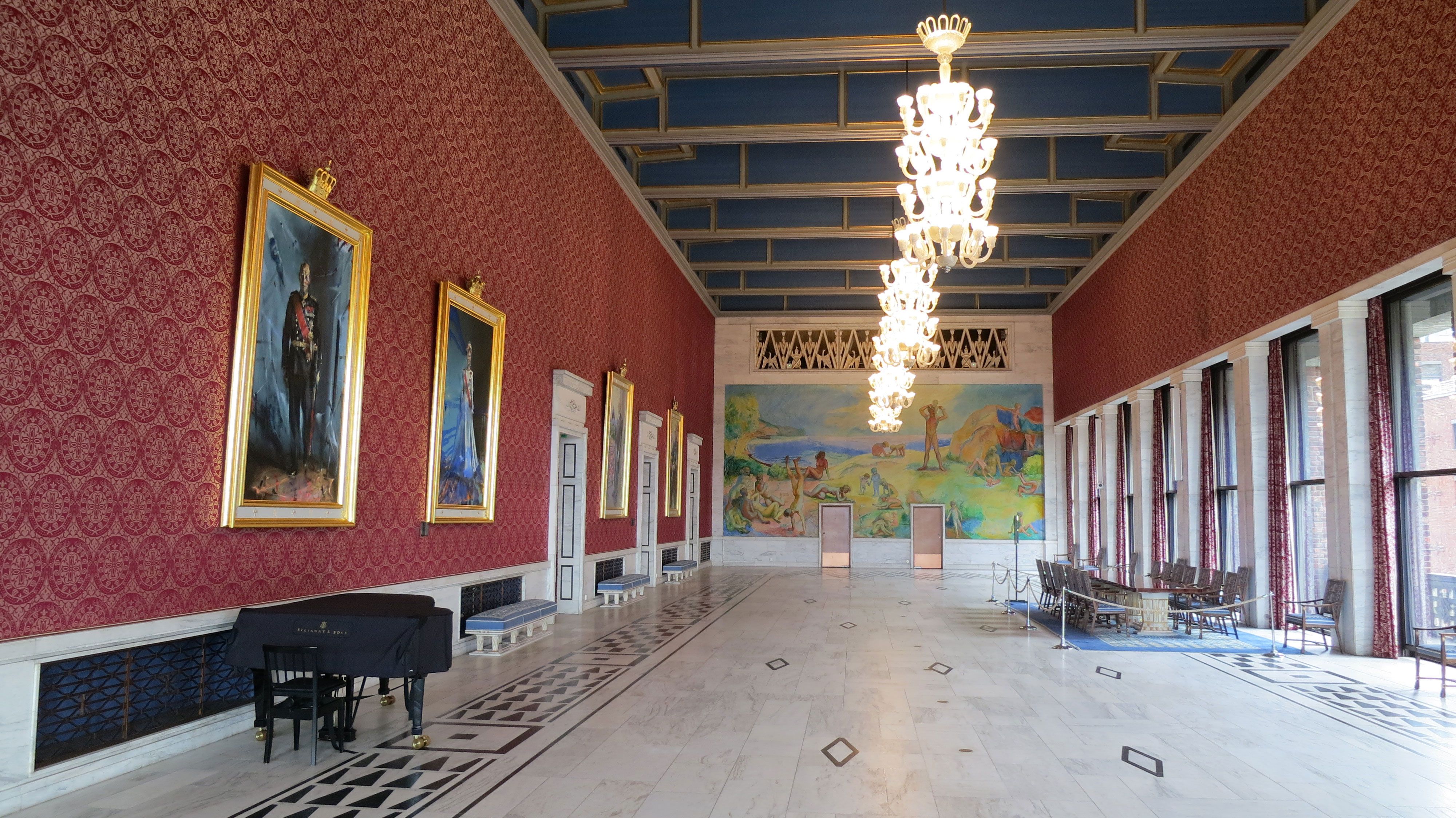 one of the hallways in oslo city hall with chandeliers from the ceiling and large paintings