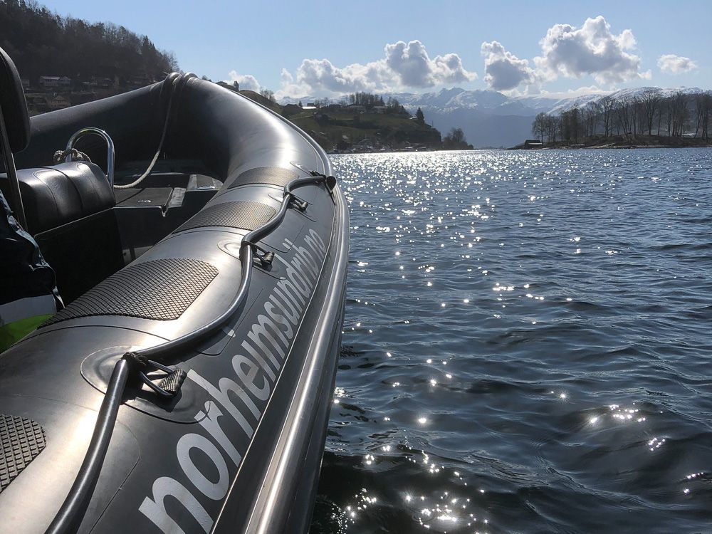 Solglitrande fjordlandskap speglar seg i ein RIB-båt frå Norheimsund RIB Seafari.