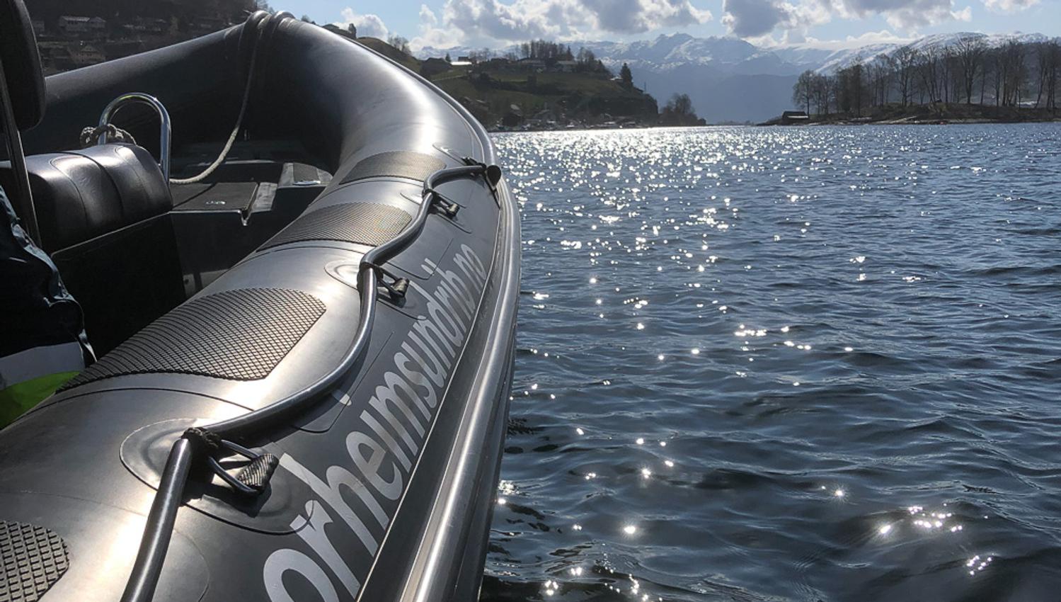 Solglitrande fjordlandskap speglar seg i ein RIB-båt frå Norheimsund RIB Seafari.