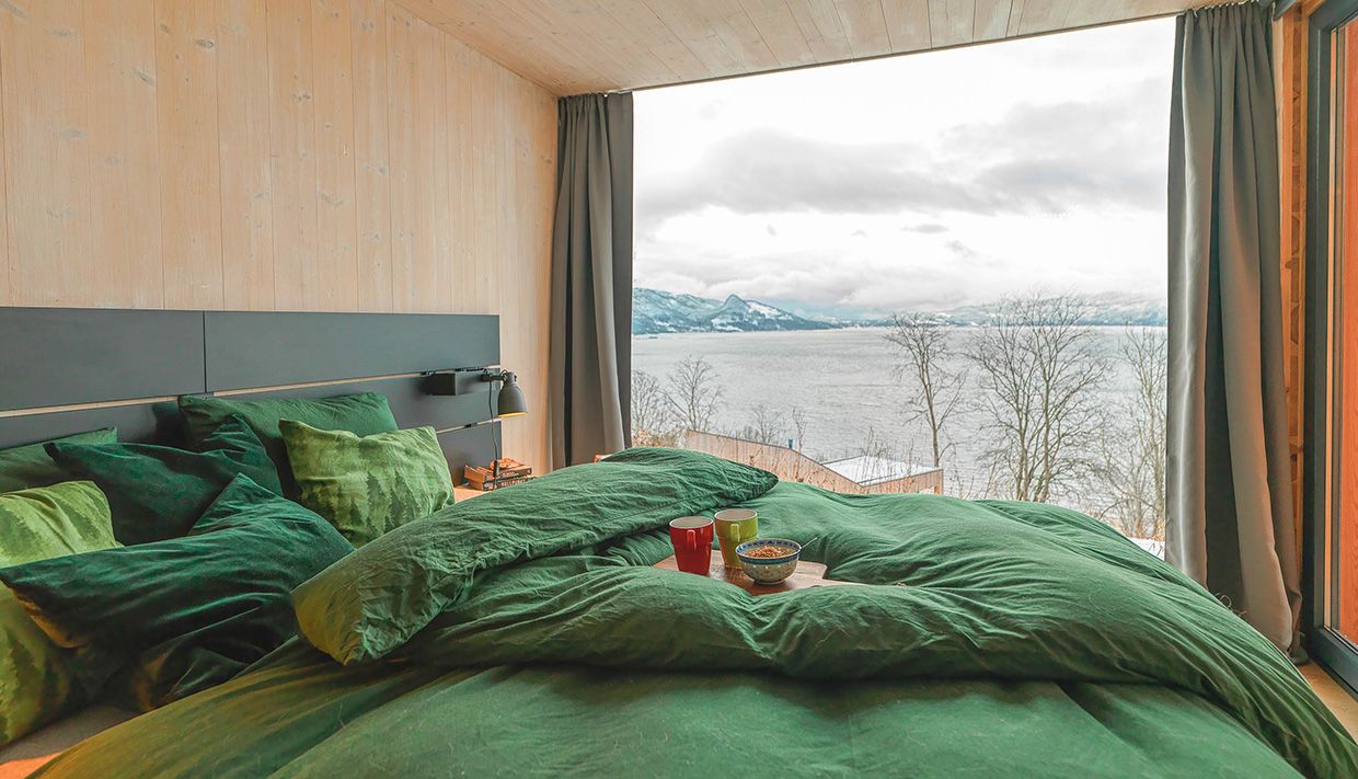 Bedroom with green bedding and views of snow-covered mountains by Hardangerfjord.