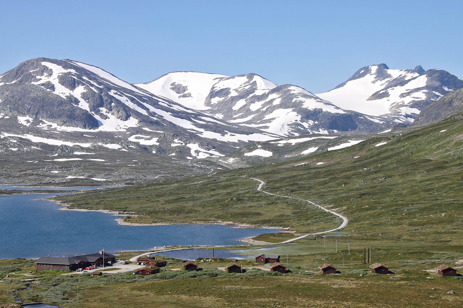 En fjellstue og et knippe hytter ved et vann i storslått høyfjellslandskap