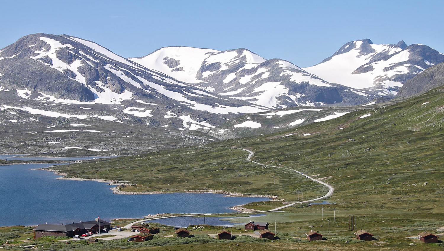 En fjellstue og et knippe hytter ved et vann i storslått høyfjellslandskap