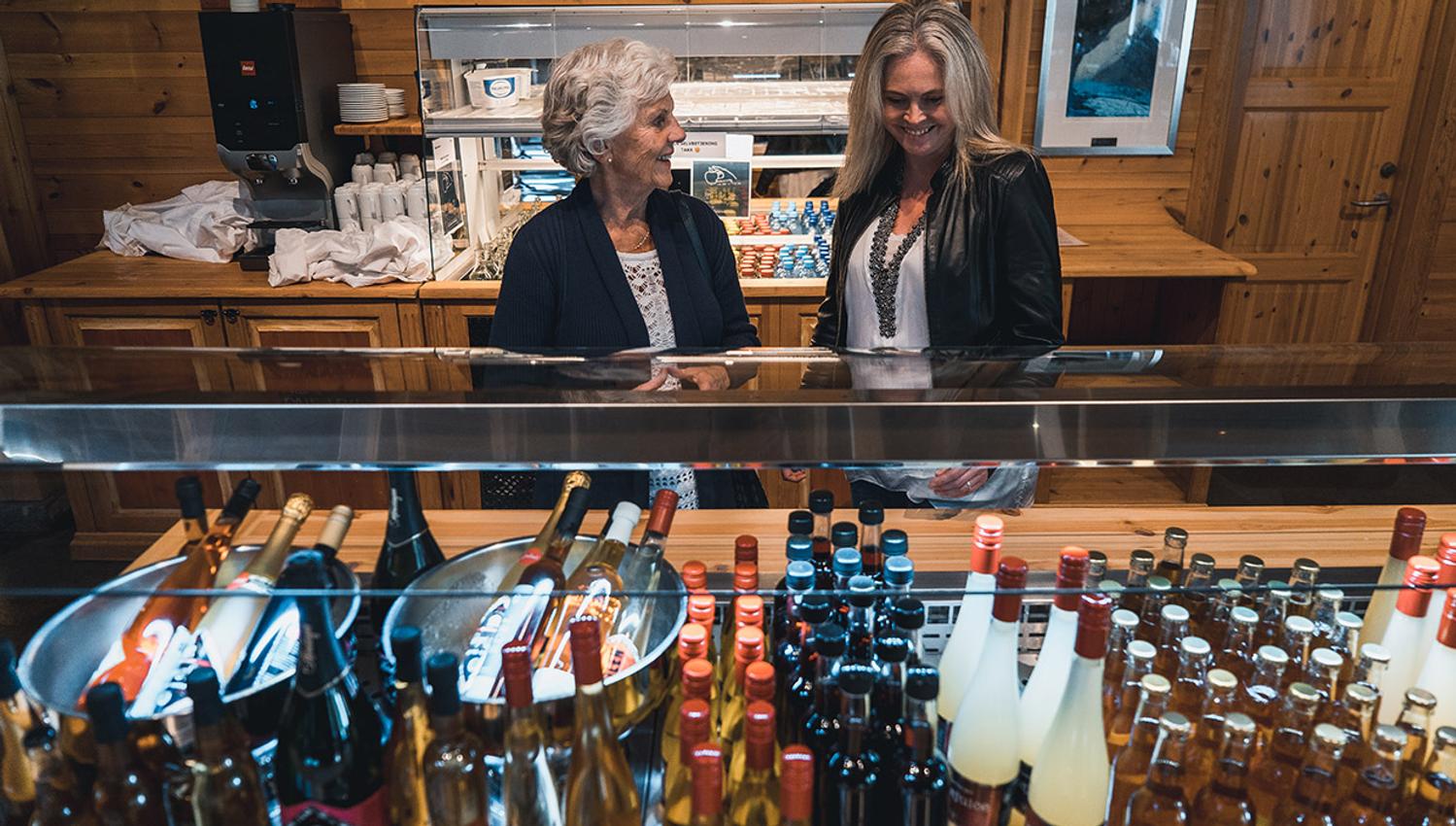 Two women looking at the display of various bottles of apple juice and other soft drinks at the Hardangerviddahallen restaurant.