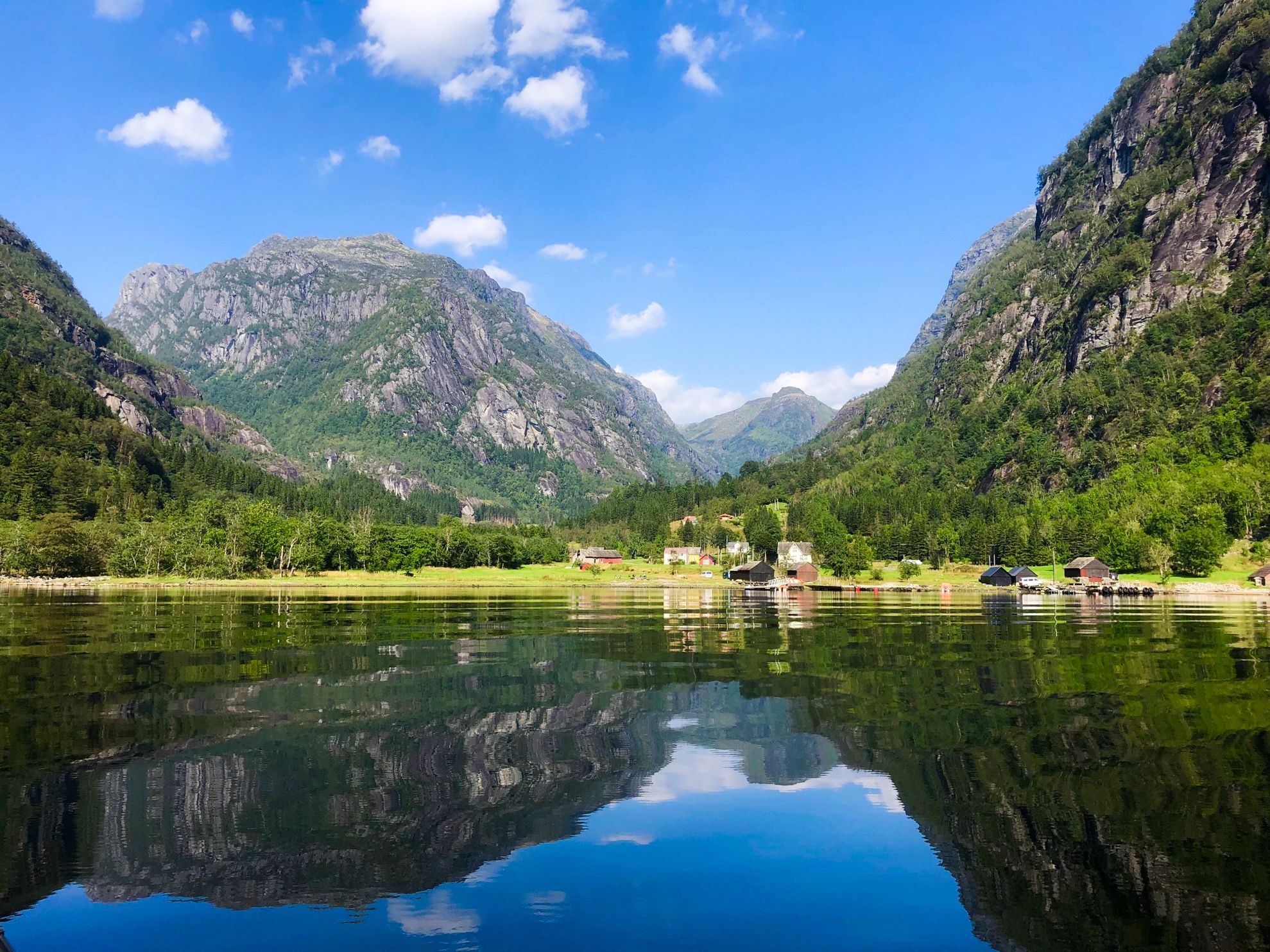 Blikkstille fjord i Hardanger, omkransa av majestetiske fjell og idylliske små gardar.