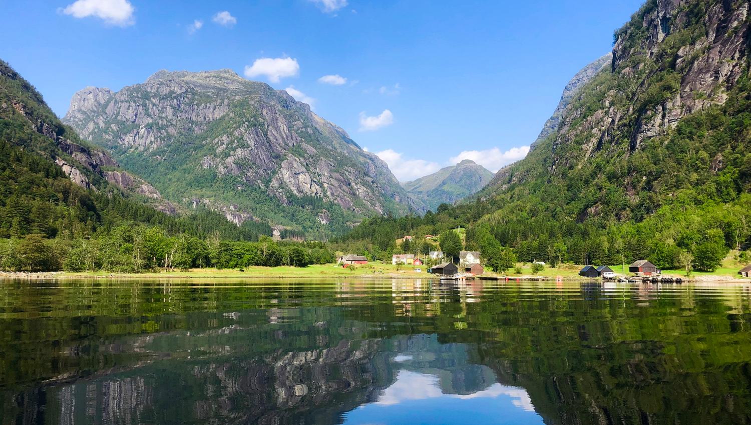 Blikkstille fjord i Hardanger, omkransa av majestetiske fjell og idylliske små gardar.