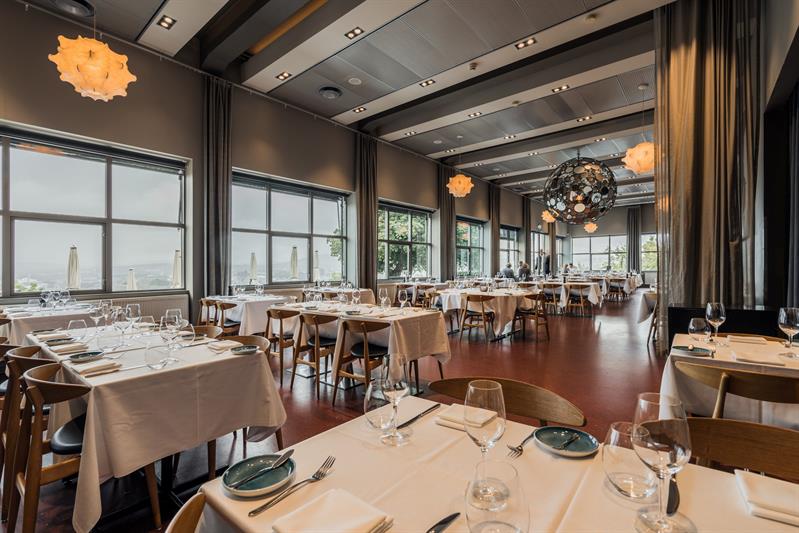 Elegant dining room with white tablecloths, large windows and contemporary lighting.