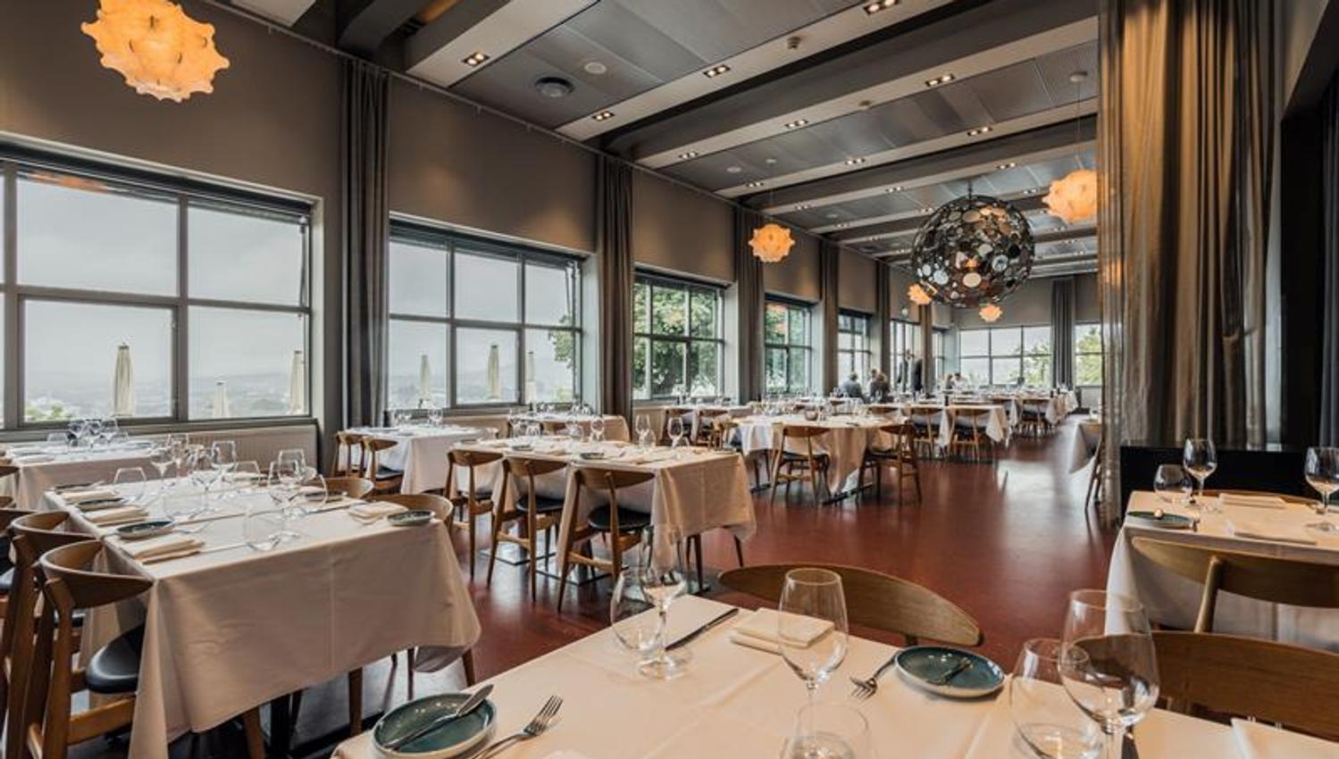 Elegant dining room with white tablecloths, large windows and contemporary lighting.