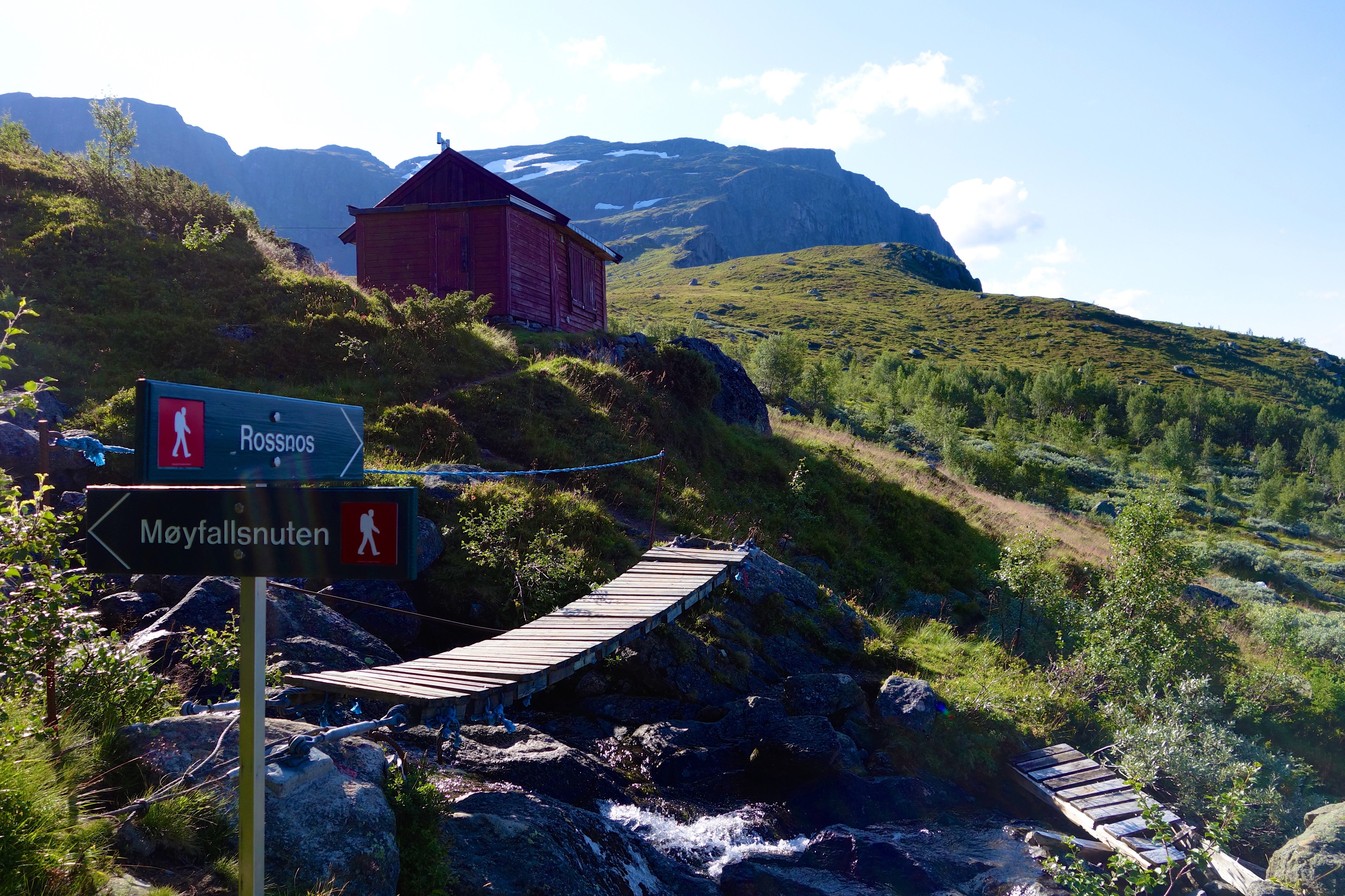 Merka tursti mot Rossnos i Hardanger med utsikt til fjell, hytte og klår sommarhimmel.