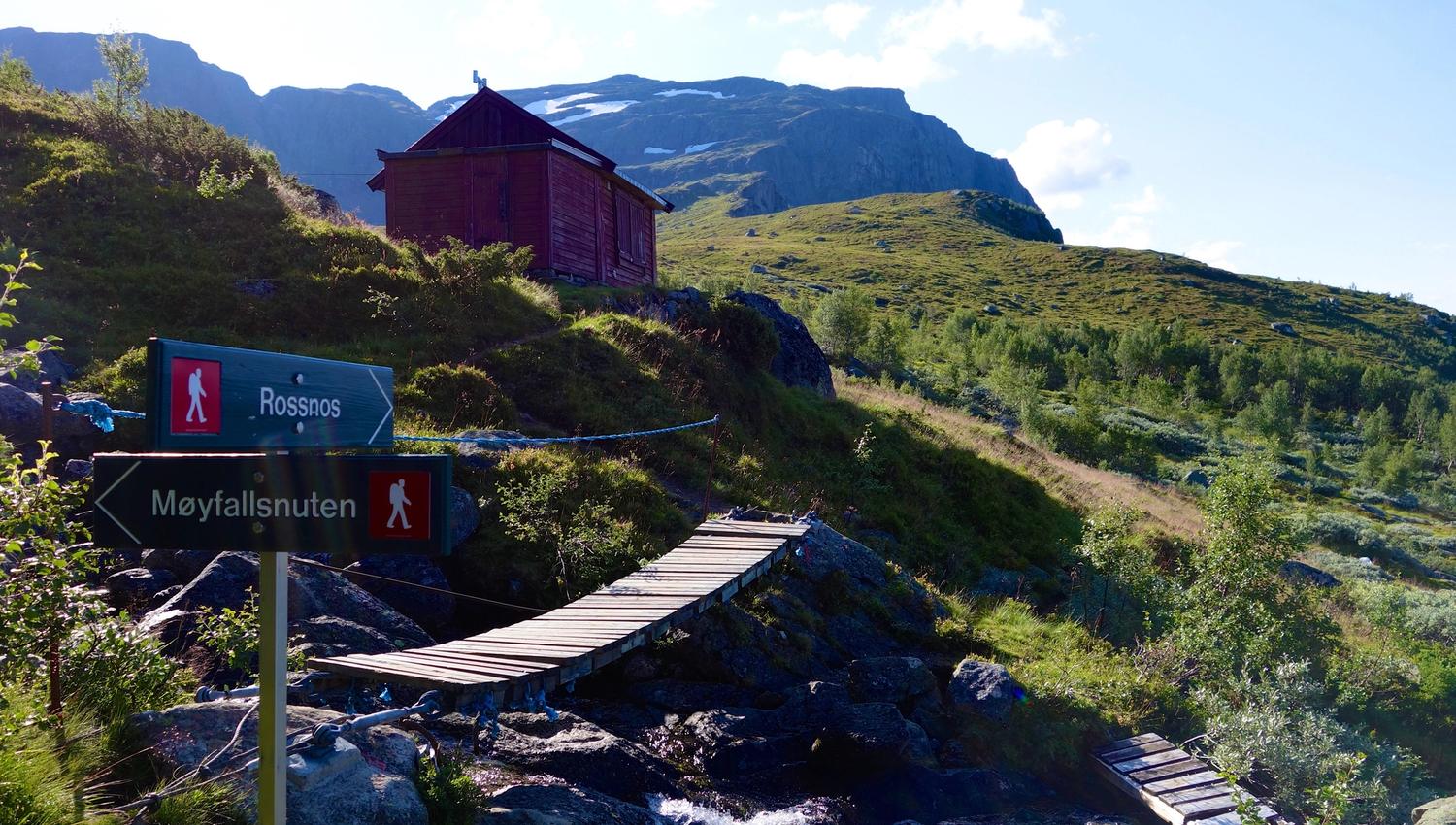Merka tursti mot Rossnos i Hardanger med utsikt til fjell, hytte og klår sommarhimmel.