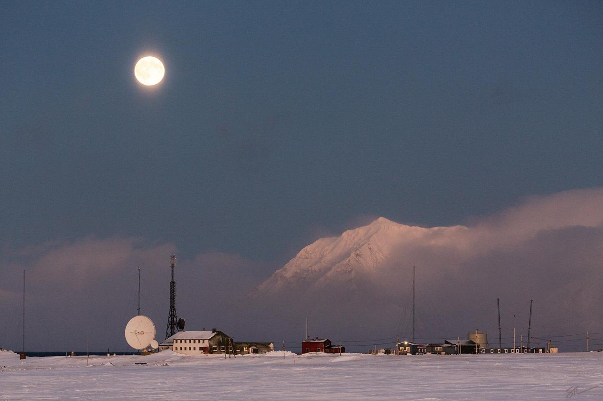 Isfjord Radio in a snowy landscape with mist over the fjord in the background and the moon shining above.