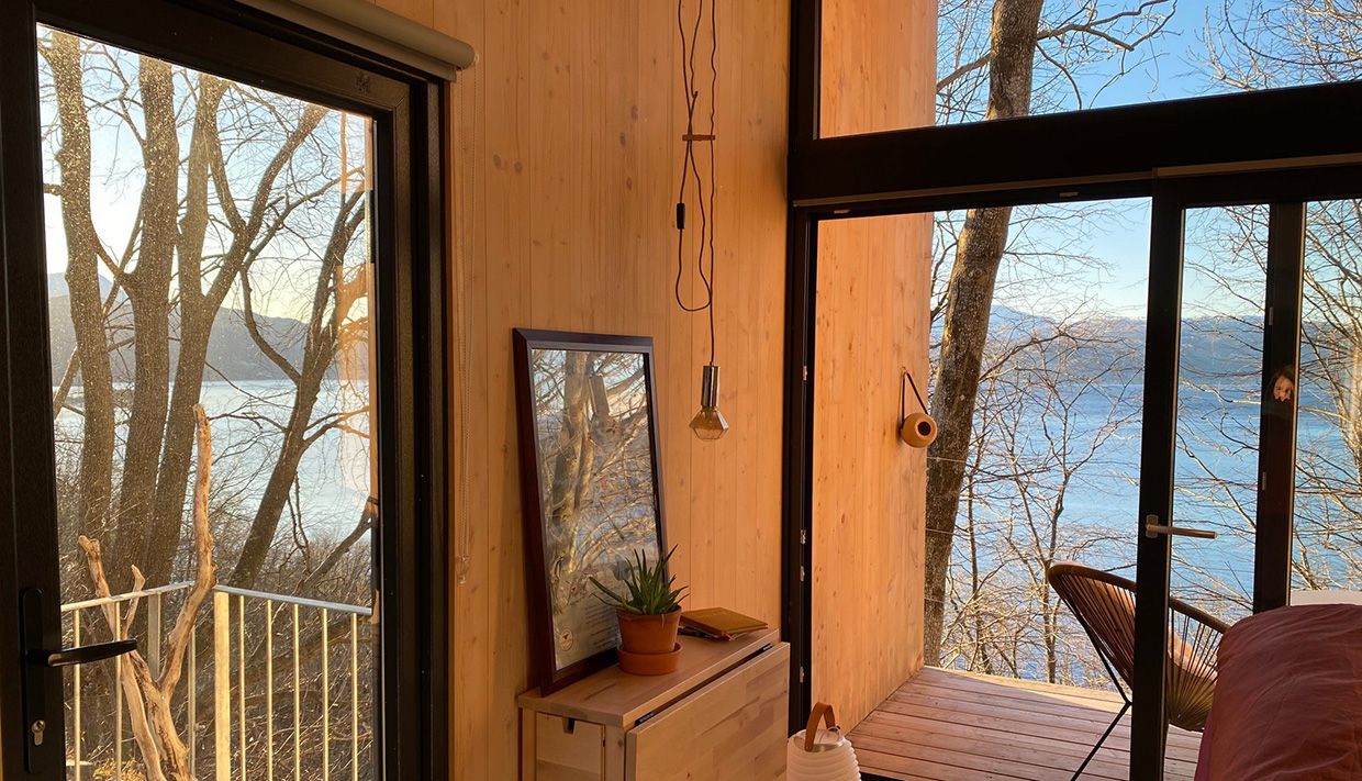 Interior of the cabin with large windows and a view of the fjord in Hardanger.