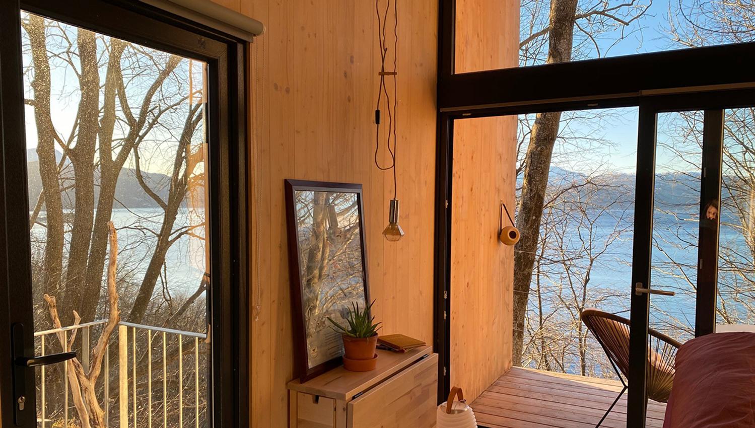 Interior of the cabin with large windows and a view of the fjord in Hardanger.