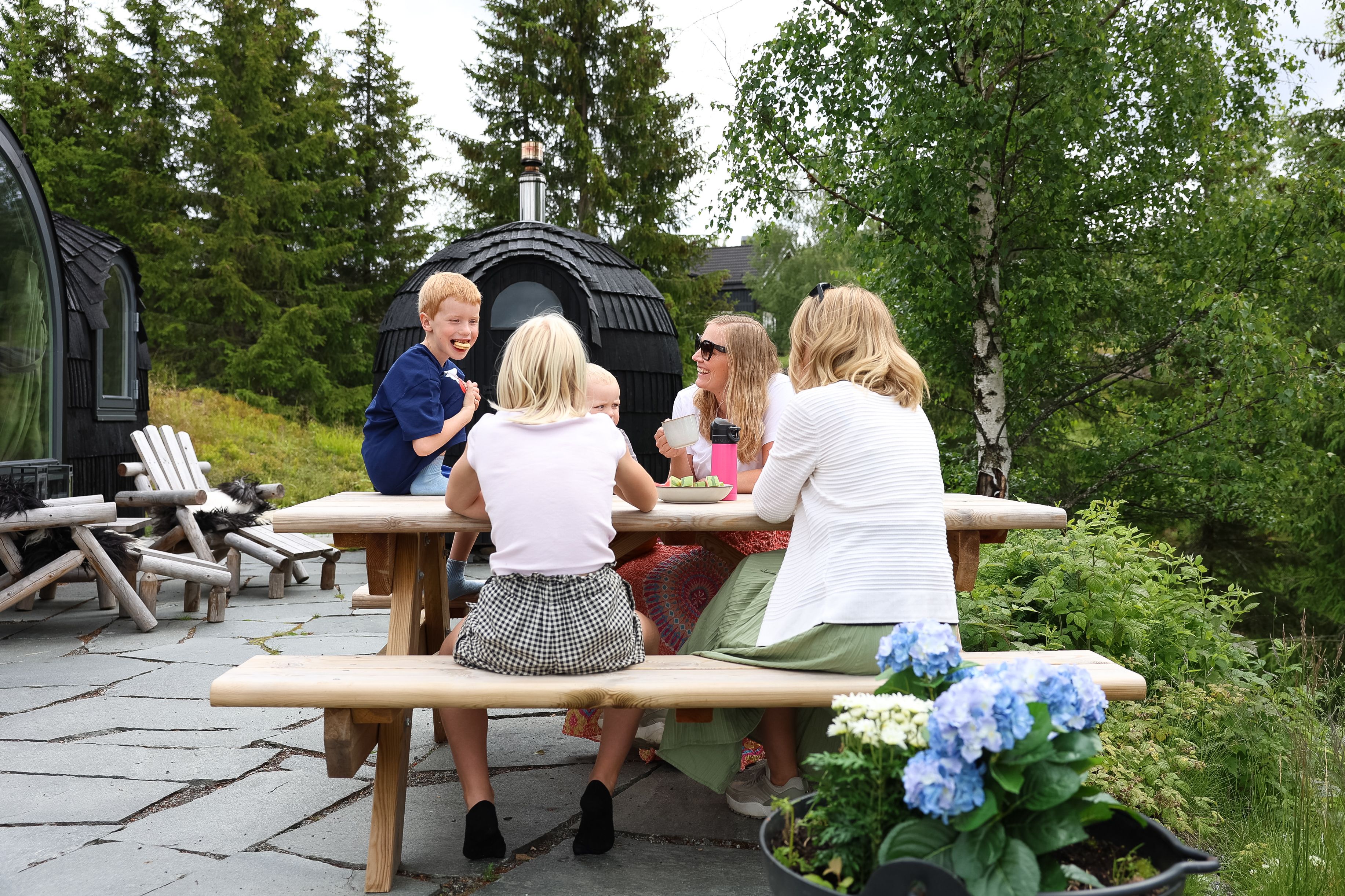 A group sitting at a picnic table outdoors near a grill hut