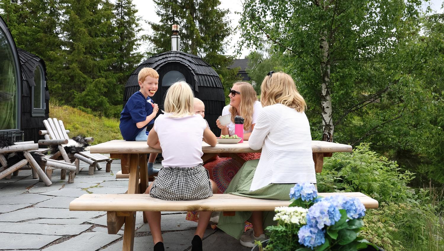 A group sitting at a picnic table outdoors near a grill hut