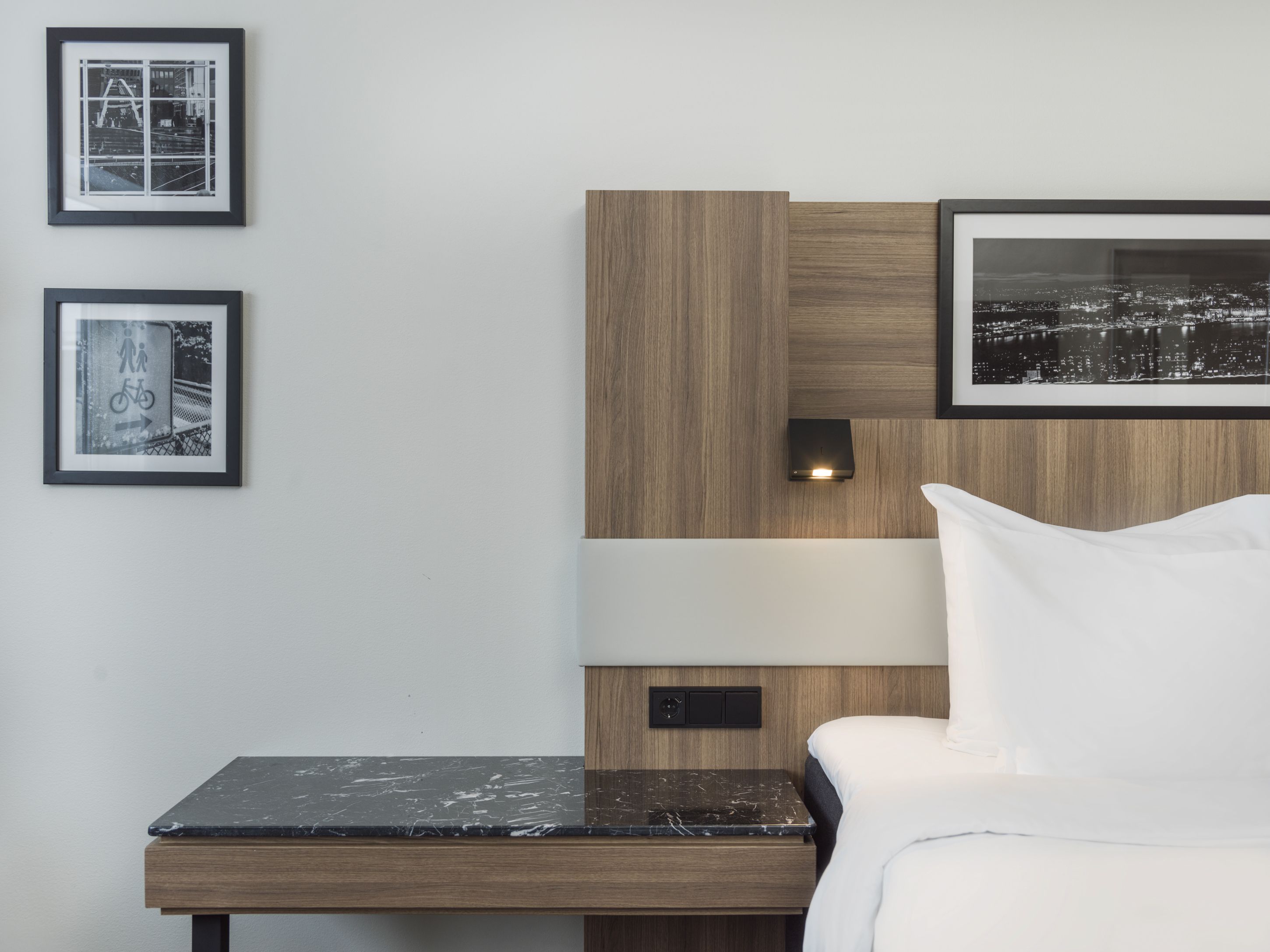 Detail from a hotel room. Bed, bedstand, black-an-white photos in frames. Photo