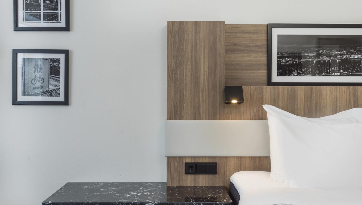Detail from a hotel room. Bed, bedstand, black-an-white photos in frames. Photo