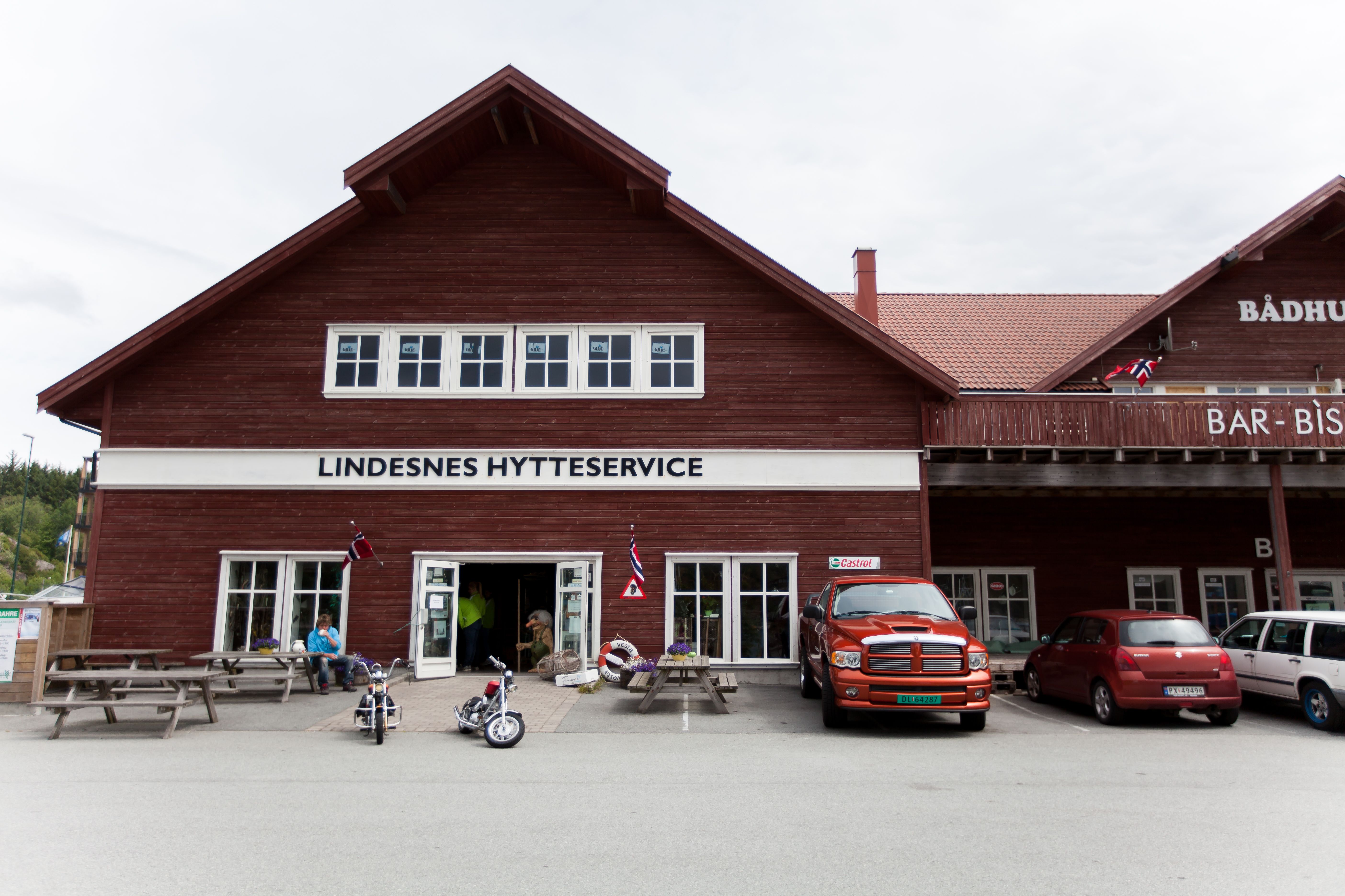 Lindesnes Hytteservice - Fasade. Brunrød bygning, med benker på utsiden
