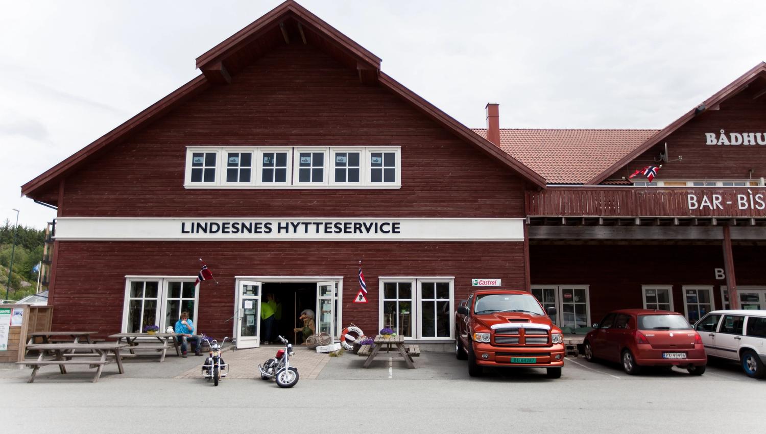 Lindesnes Hytteservice - Fasade. Brunrød bygning, med benker på utsiden