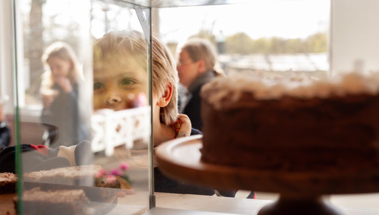 Et barn ser i et vitrinenskap med kake