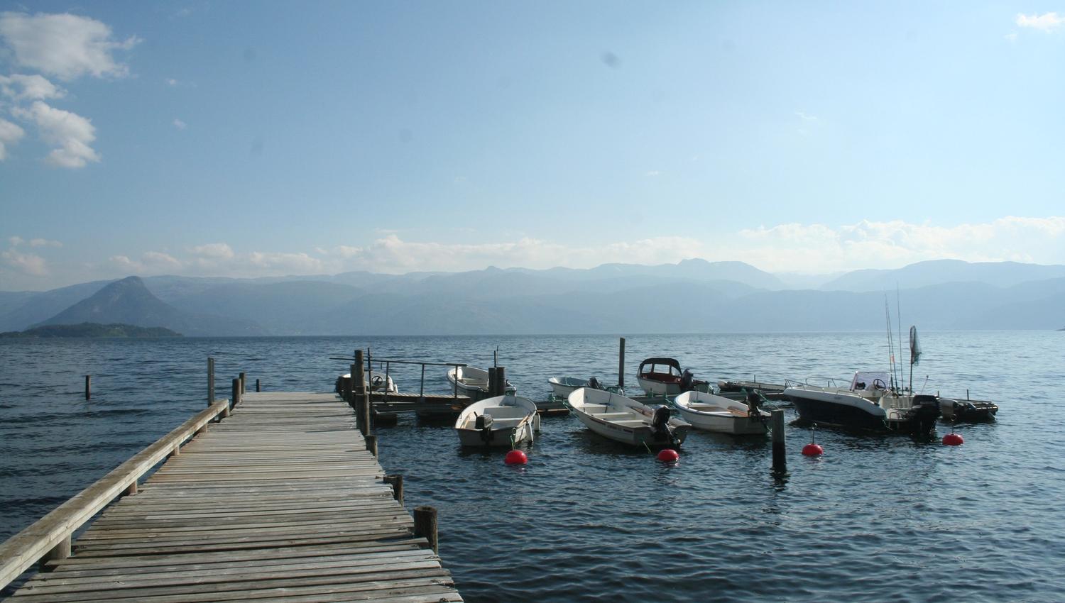 Brygge med småbåtar ved Hardanger Feriesenter med fjell og fjordlandskap.