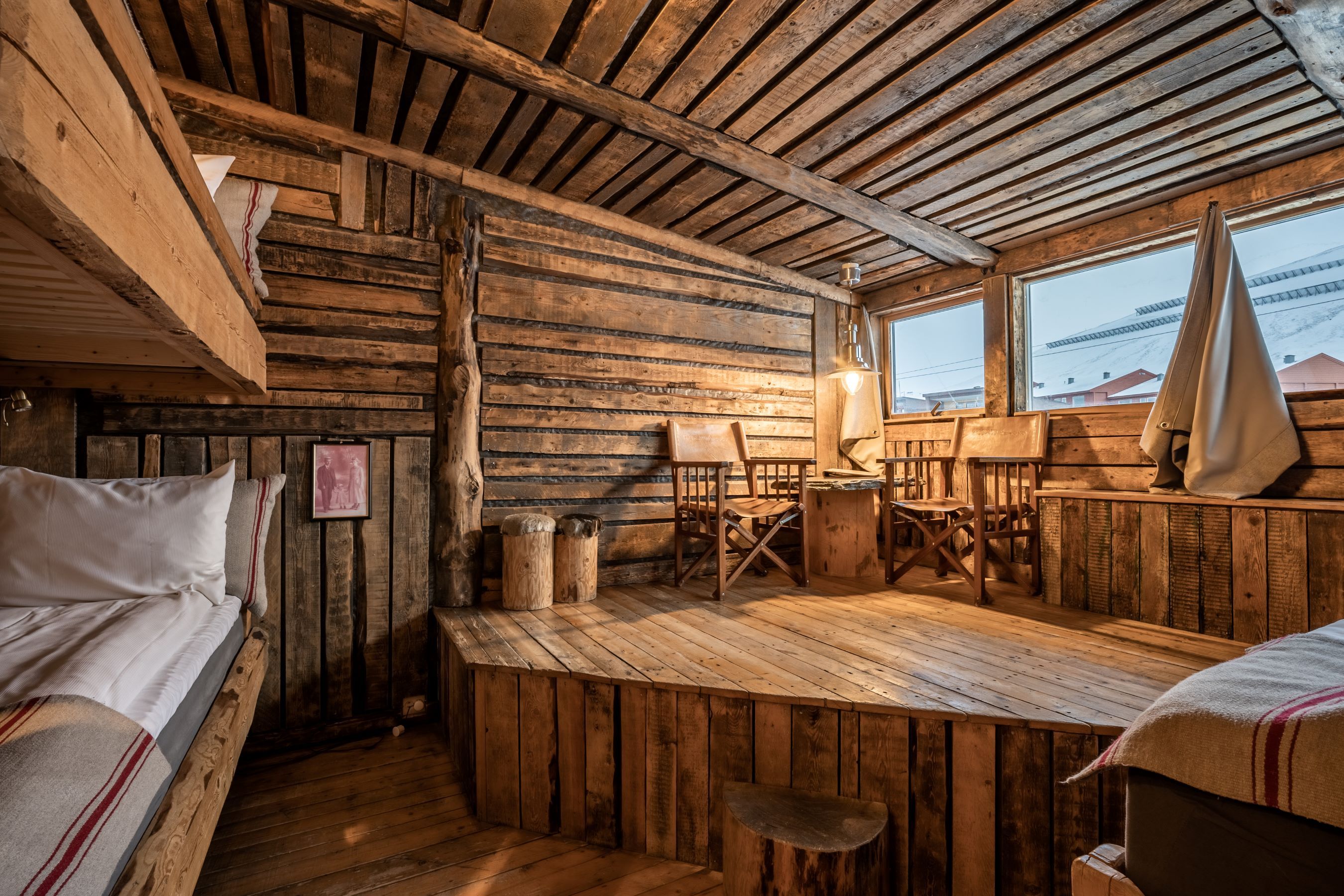A cabin inspired hotel room, with three beds and two chairs.