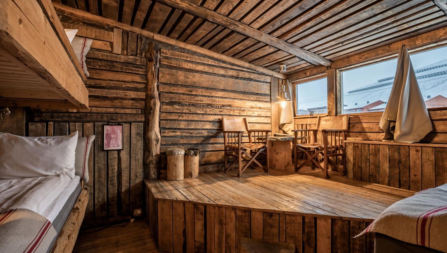 A cabin inspired hotel room, with three beds and two chairs.