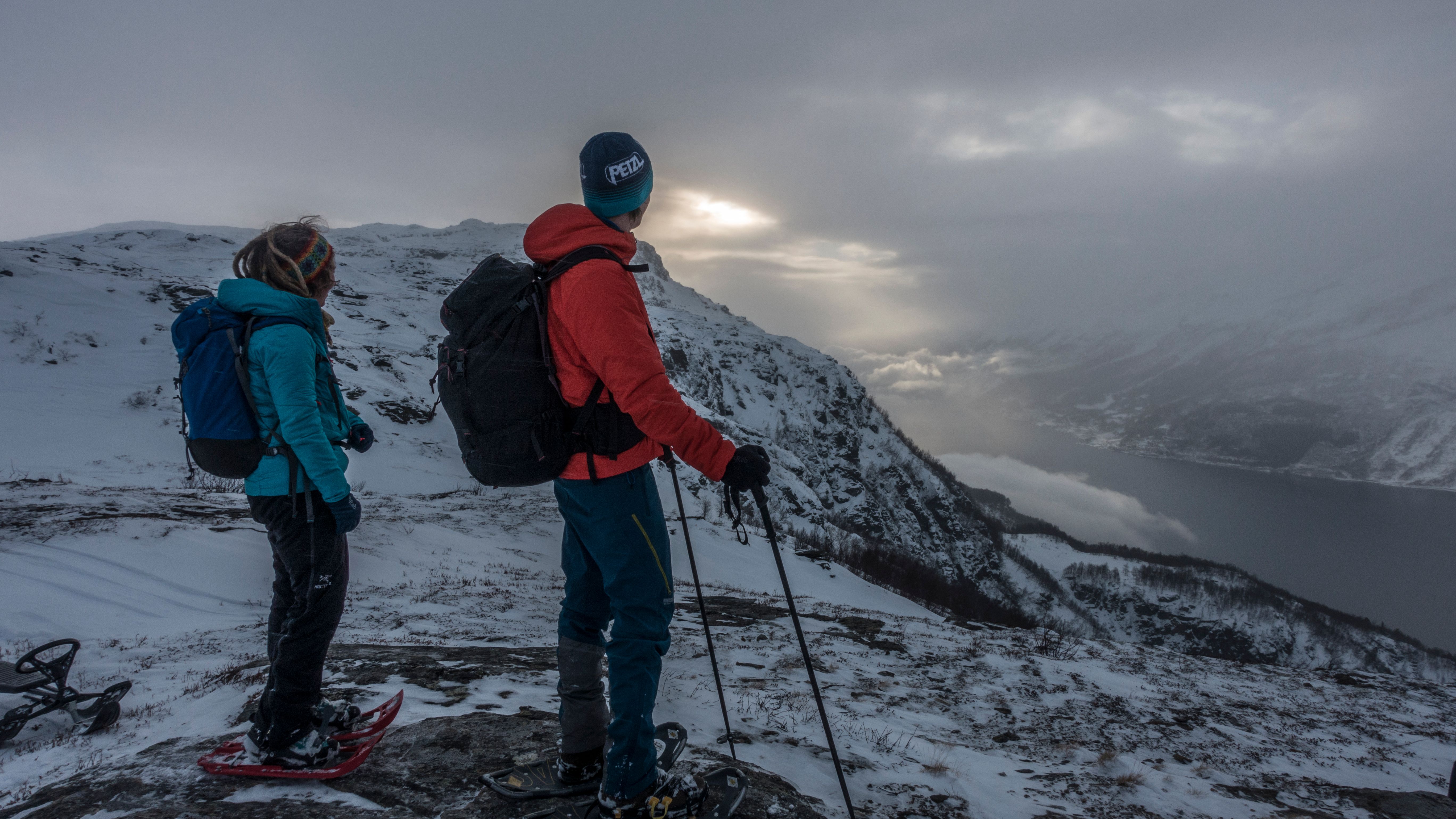 Snowshoers pausing to admire sunlight breaking over the fjord and winter mountains.