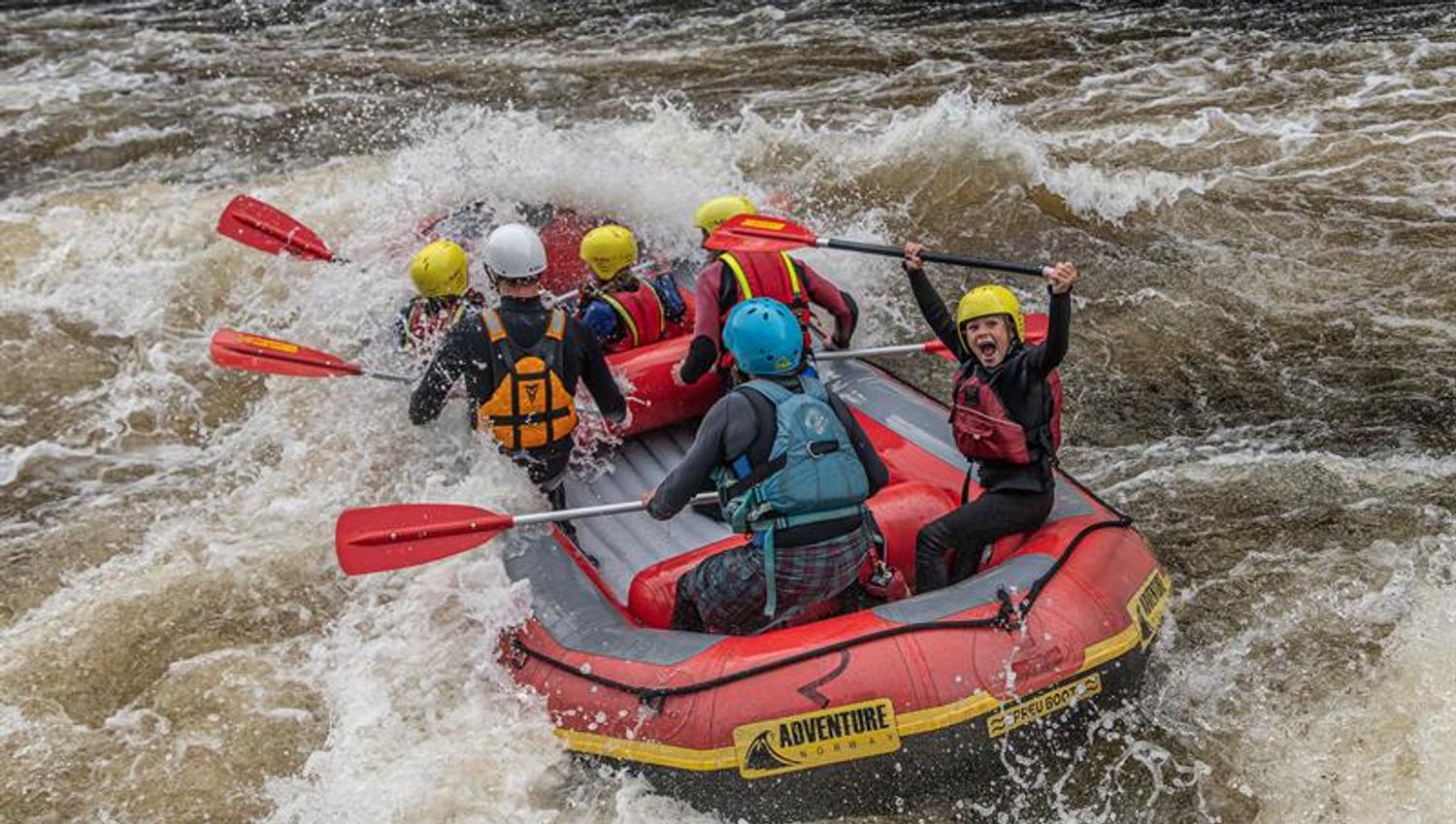 Rafting i Mandalselva, en glad gjeng i bølgene. Et barn som roper av glede og løfter åren over hodet