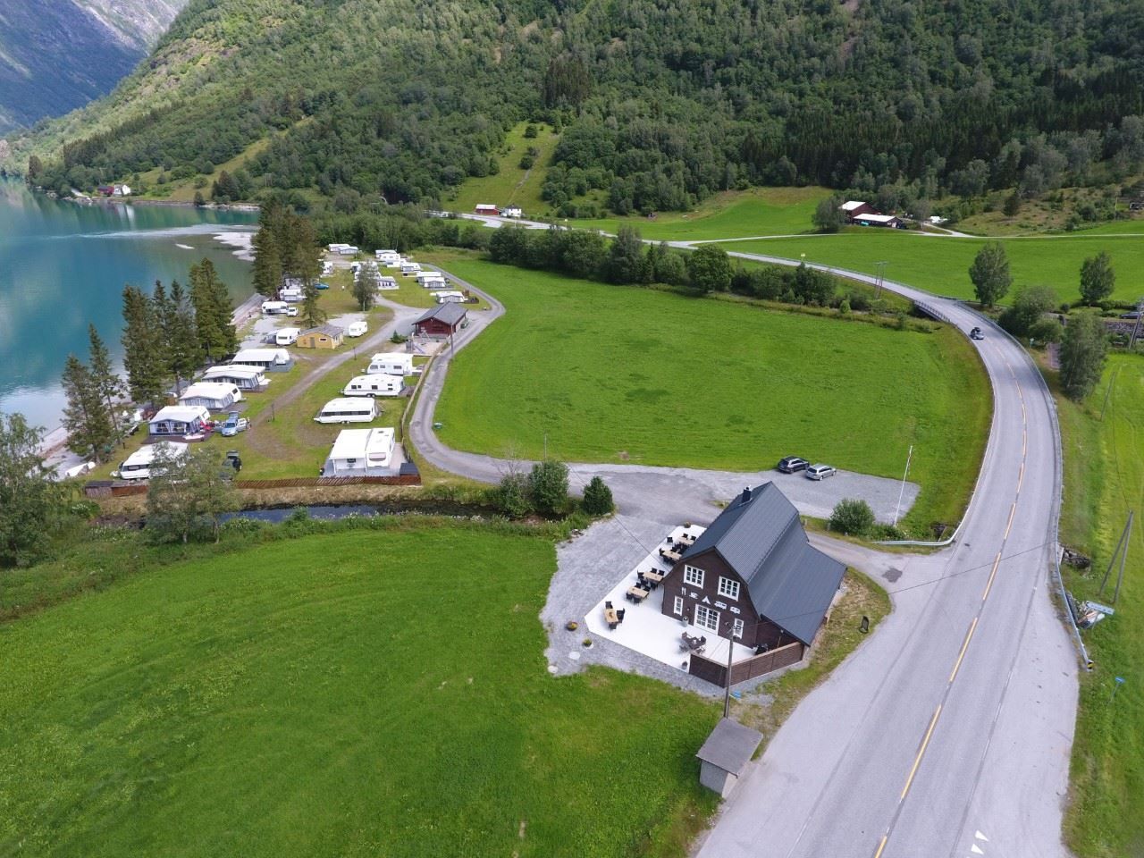Droneutsikt over Grande Camping ved Oppstrynsvatnet i Oppstryn, omgitt av fjell og den blågrøne fargen frå brevatnet.
