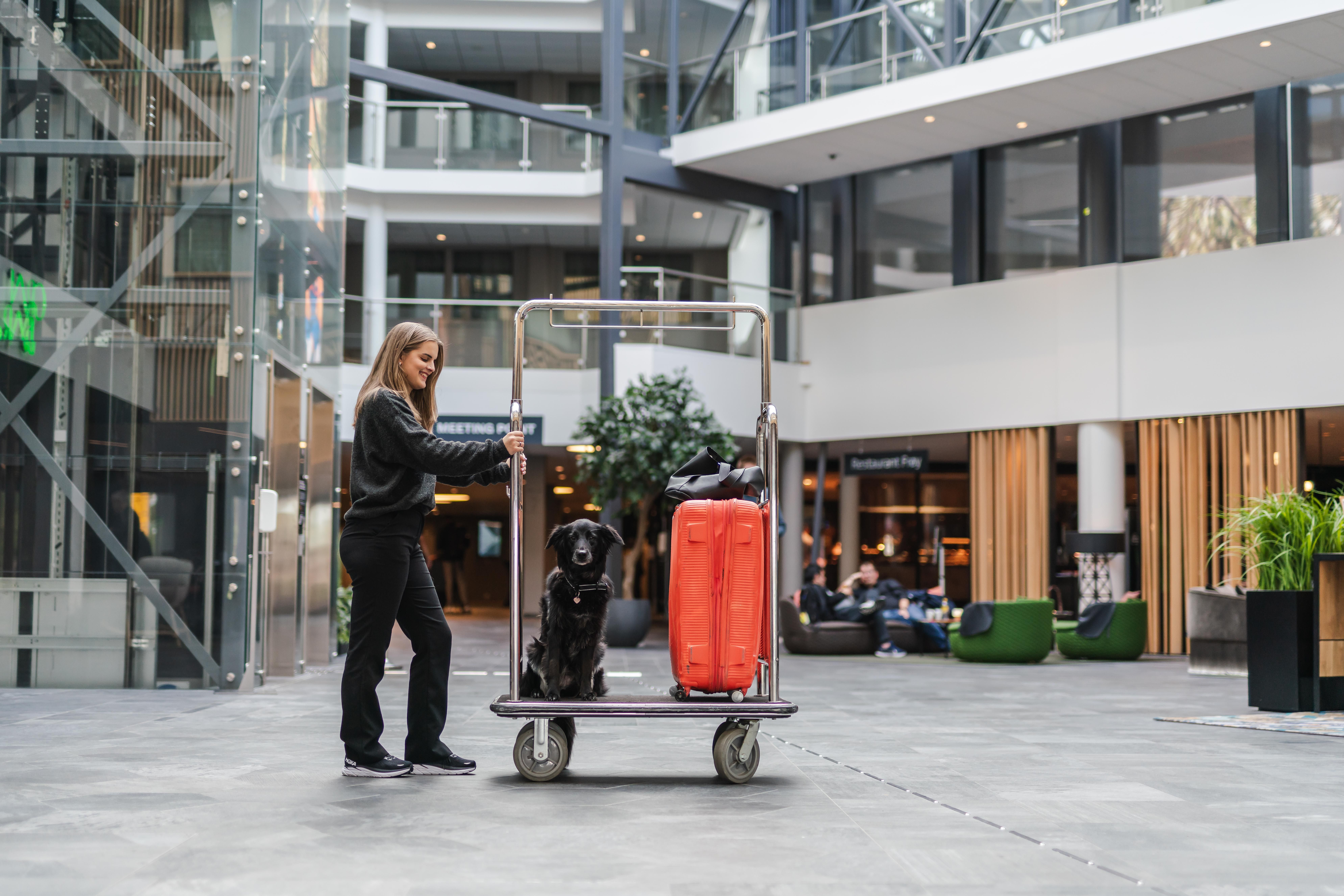 Dame som skyver en trallee ed en rød koffert, en hun i en lobby på et hotell
