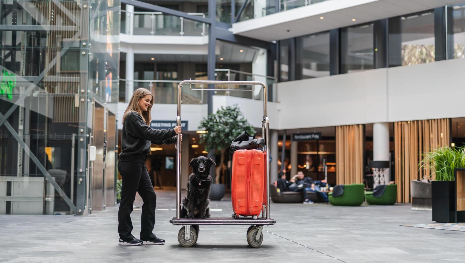 Dame som skyver en trallee ed en rød koffert, en hun i en lobby på et hotell
